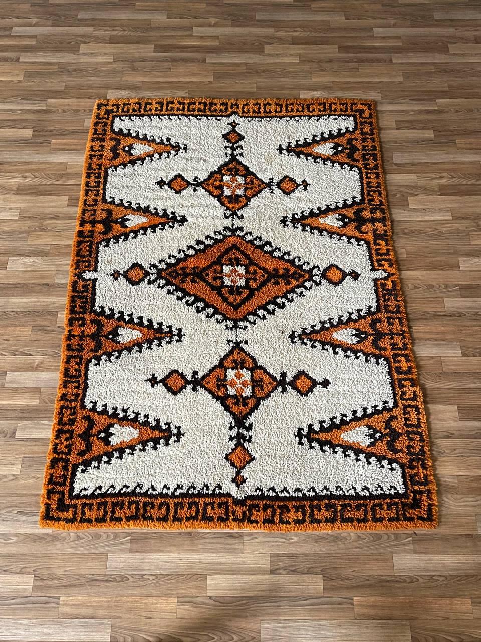 Condition: Original Vintage Condition

Materials: Hand-Woven Wool
Dimensions: 0.50”H x 80.50”W x 56”D

This stunning vintage shag rug from the 1970s showcases a bold geometric tribal pattern in warm tones of orange, black, and cream. Hand-woven from