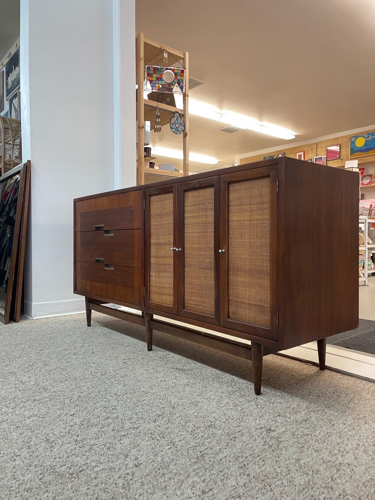 This Dresser has 3 Drawers with Silver Toned Handles and Beautiful wood Inlay Features. Next to this, there are Cane Accented Doors Opening to Cabinet Space as well as Three Additional Drawers as Shown. Walnut Toned Wood. The Top of this Drawer has