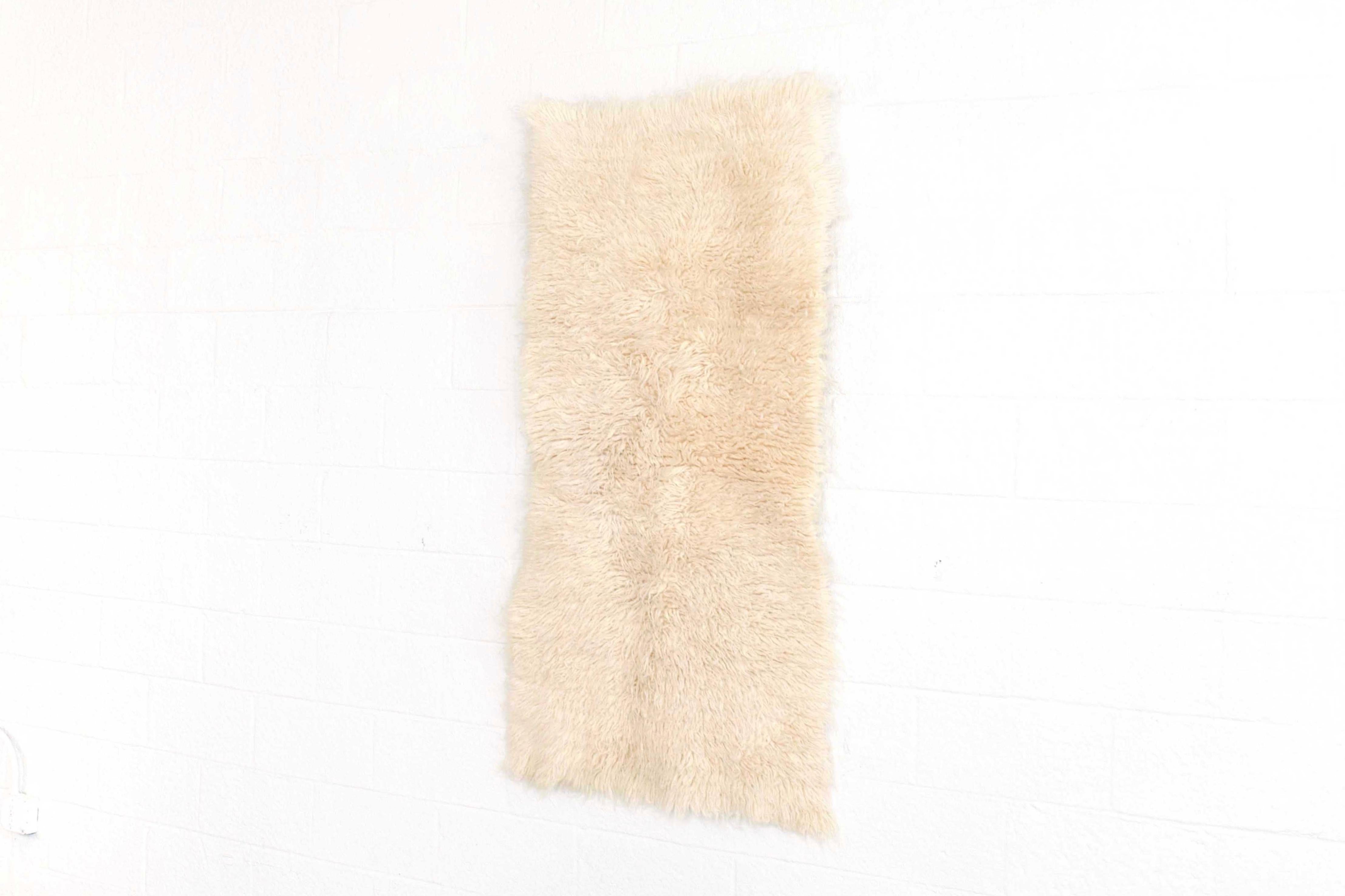 This small vintage wool shag rug circa 1960 is handwoven from 100% un-dyed wool and has a soft and luxurious thick shaggy pile. The clean, Minimalist design of this natural ivory carpet makes it the perfect accent for any contemporary style of
