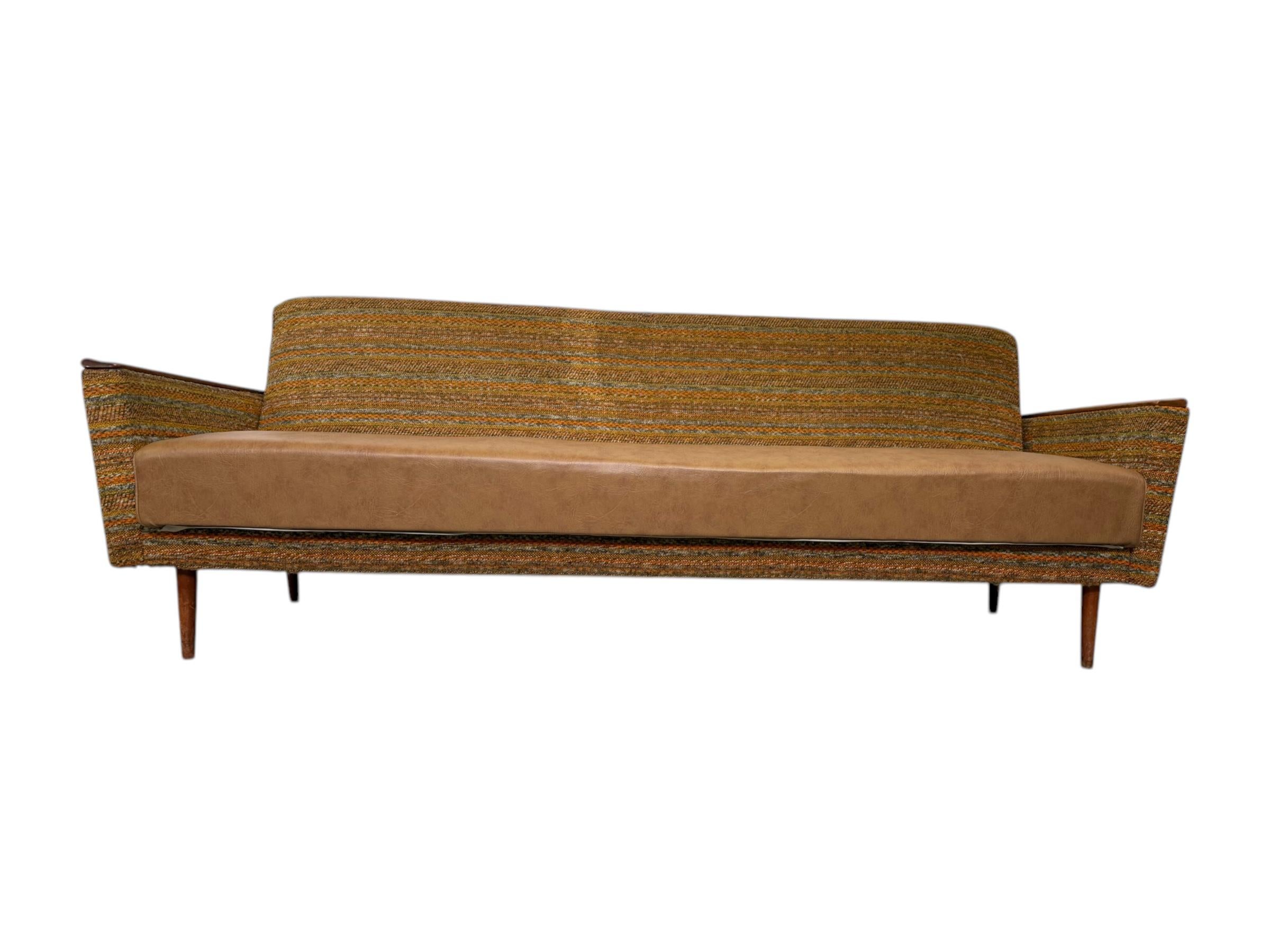  This mid-century modern sofa, likely from the 1950s or 1960s, showcases a minimalist silhouette with clean, straight lines, a low backrest, and narrow, angled arms capped with wooden trim, all elevated on slender teak legs that give it a light,