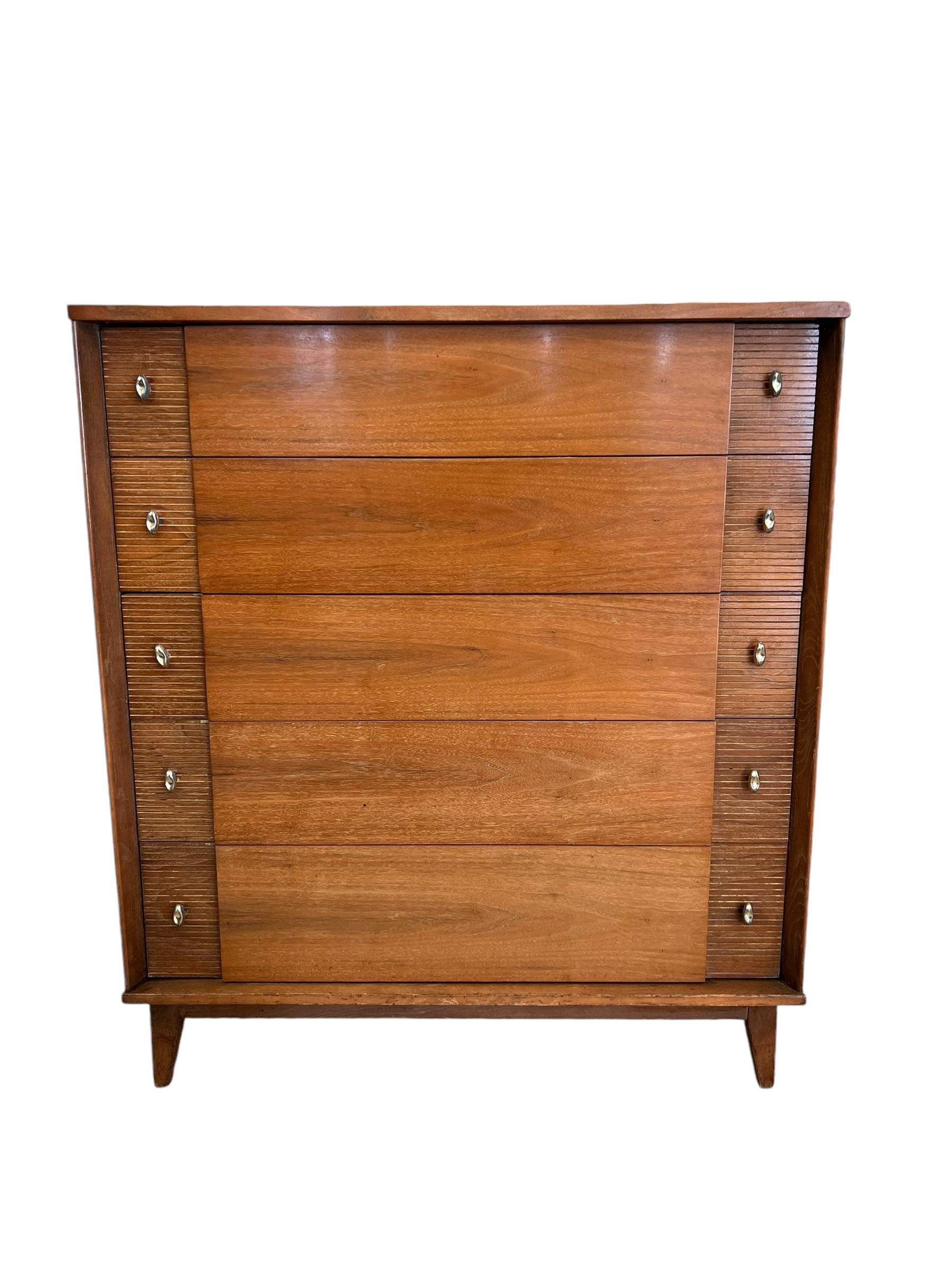 Questo elegante comò vintage moderno è caratterizzato da una finitura in noce e da una spaziosa configurazione a cinque cassetti che offre una grande quantità di spazio per la camera da letto. Le linee pulite e moderne del design di metà secolo sono