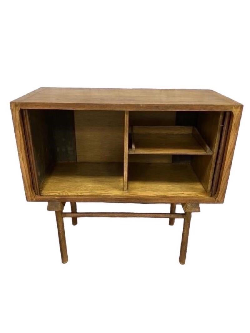 This unique vintage mid century modern record cabinet is features tambour doors that slide into the body of the case to reveal your favorite albums. Constructed of solid oak wood.  This cabinet is in good condition and the tambour doors slide