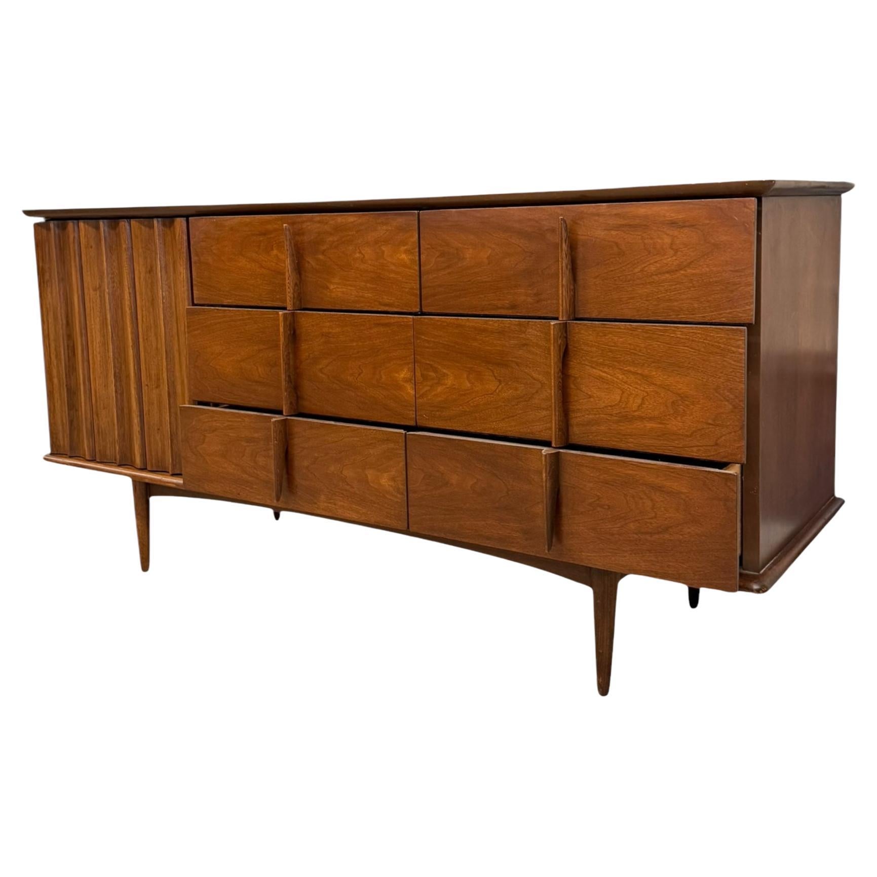 Diese 9-schübige Kommode im Vintage-Stil aus der Mitte des Jahrhunderts ist eine atemberaubende Verkörperung des Designs der 1950er bis 1970er Jahre. Sie ist mit einem satten Nussbaum- oder einem ähnlichen Hartholz-Finish versehen, das die