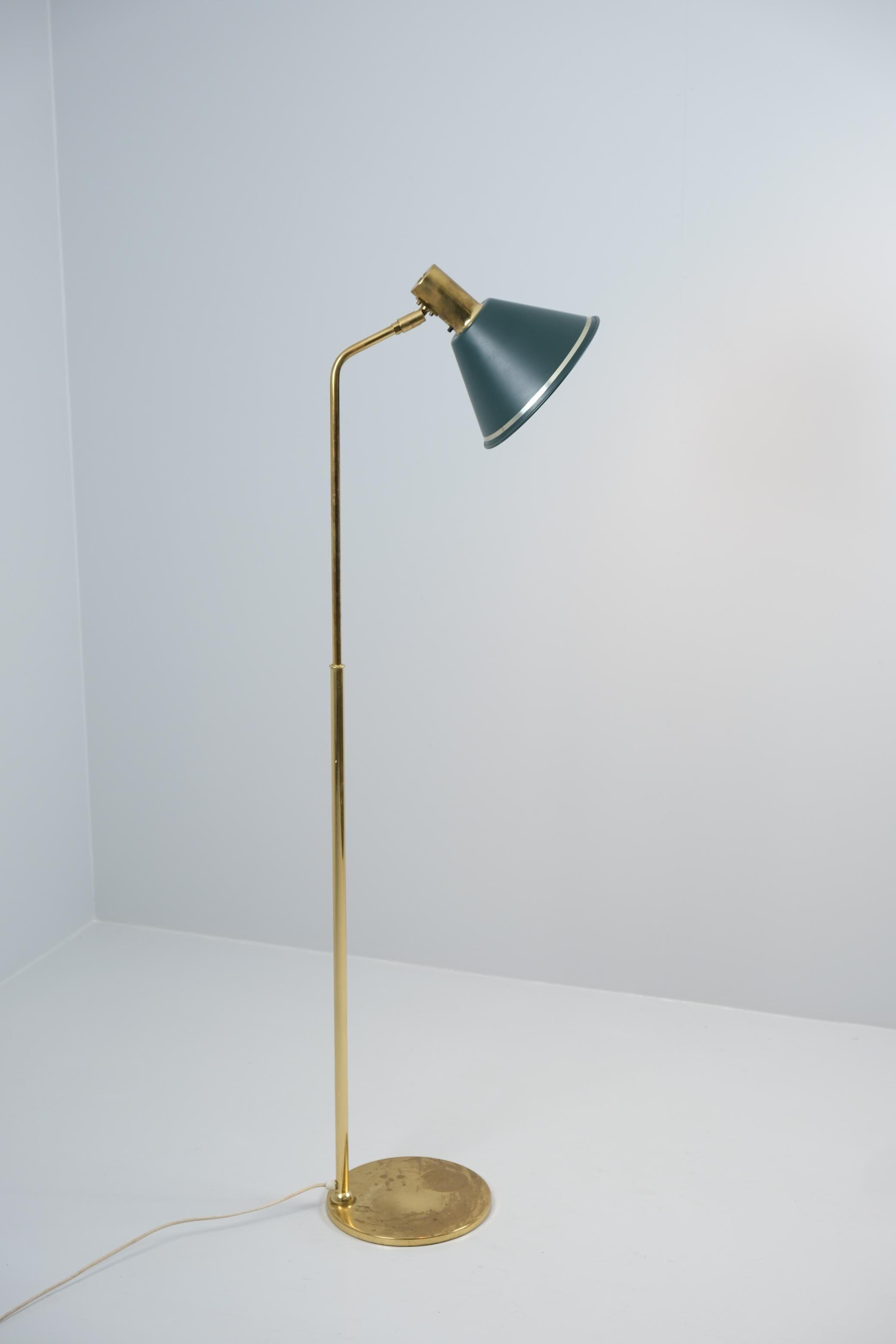 A sleek vintage floor lamp in brass and green shade by Öia. The forest green lamp shade is adjustable and has a golden stripe matching the full brass body of the lamp. The lamp is in its original condition and has the manufacturer's label to the