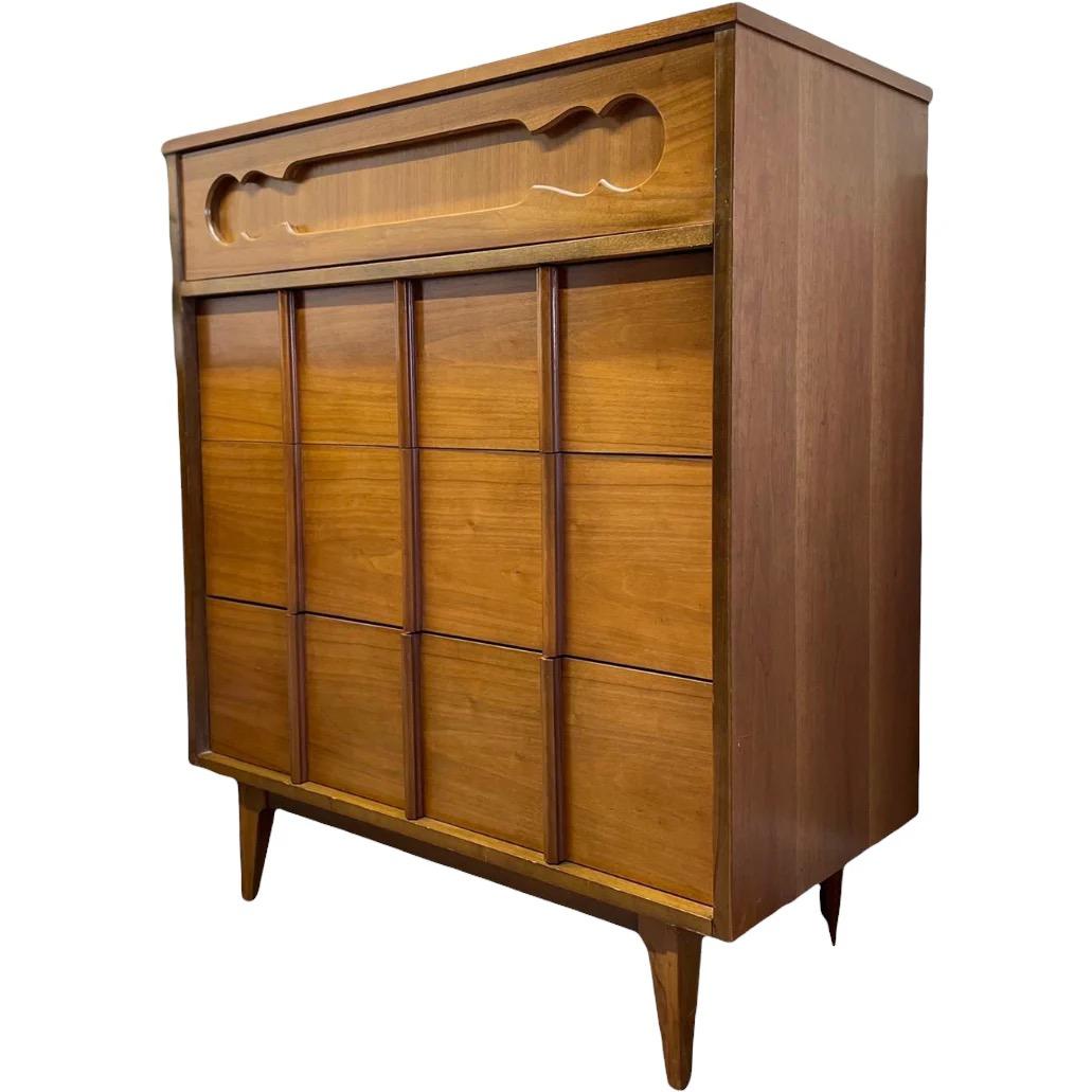  Un comò vintage di metà secolo moderno che presenta audaci frontali scultorei e linee pulite e geometriche. Il cassetto superiore è impreziosito da un dettaglio di design intagliato, mentre i cassetti inferiori sono incorniciati da pannelli
