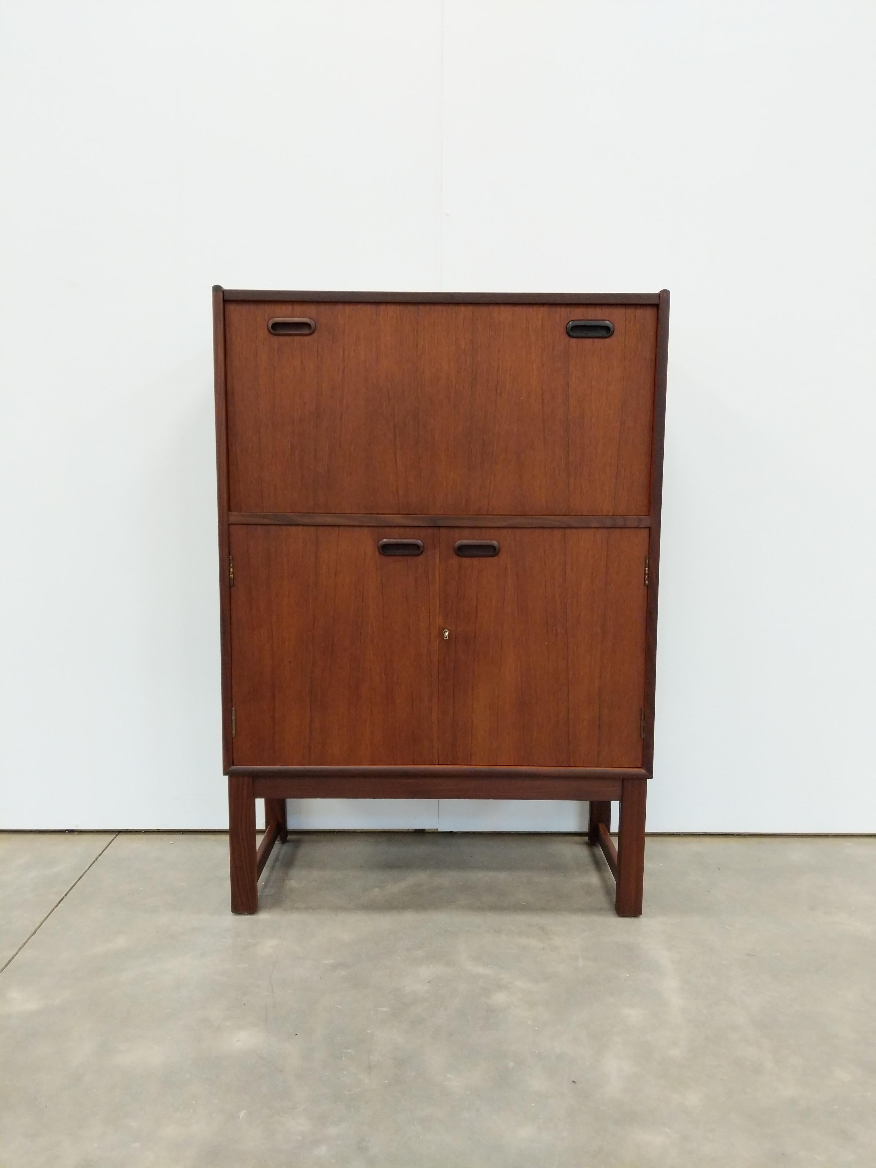 Auténtico mueble bar vintage de teca moderno de mediados de siglo.

Esta pieza está en excelentes condiciones de acabado, con pocos signos de desgaste relacionado con la edad (ver fotos).

La sección frontal abatible se abre en tándem con la sección