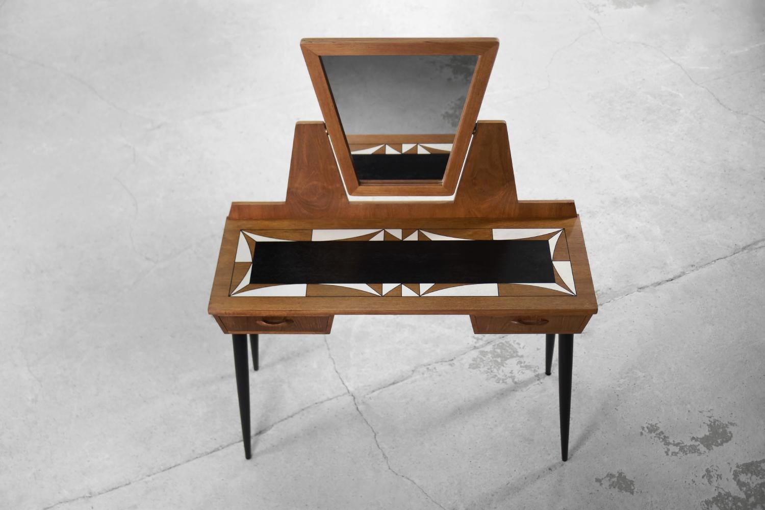 The modernist dressing table with a mirror was made in Scandinavia during the 1960s. It is finished with teak wood in a warm shade of brown. It has two drawers. A mirror is in a geometric frame, the angle of which can be freely adjusted. The