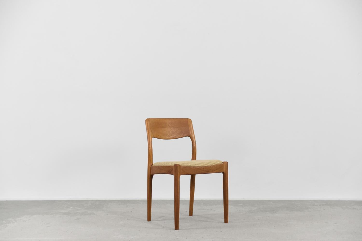 This modernist dining chair was designed by Juul Kristensen for the Danish manufacture JK Denmark during the 1960s. The chair is made of solid teak wood in a warm shade of brown and strong graining. The contoured backrest smoothly blends with the