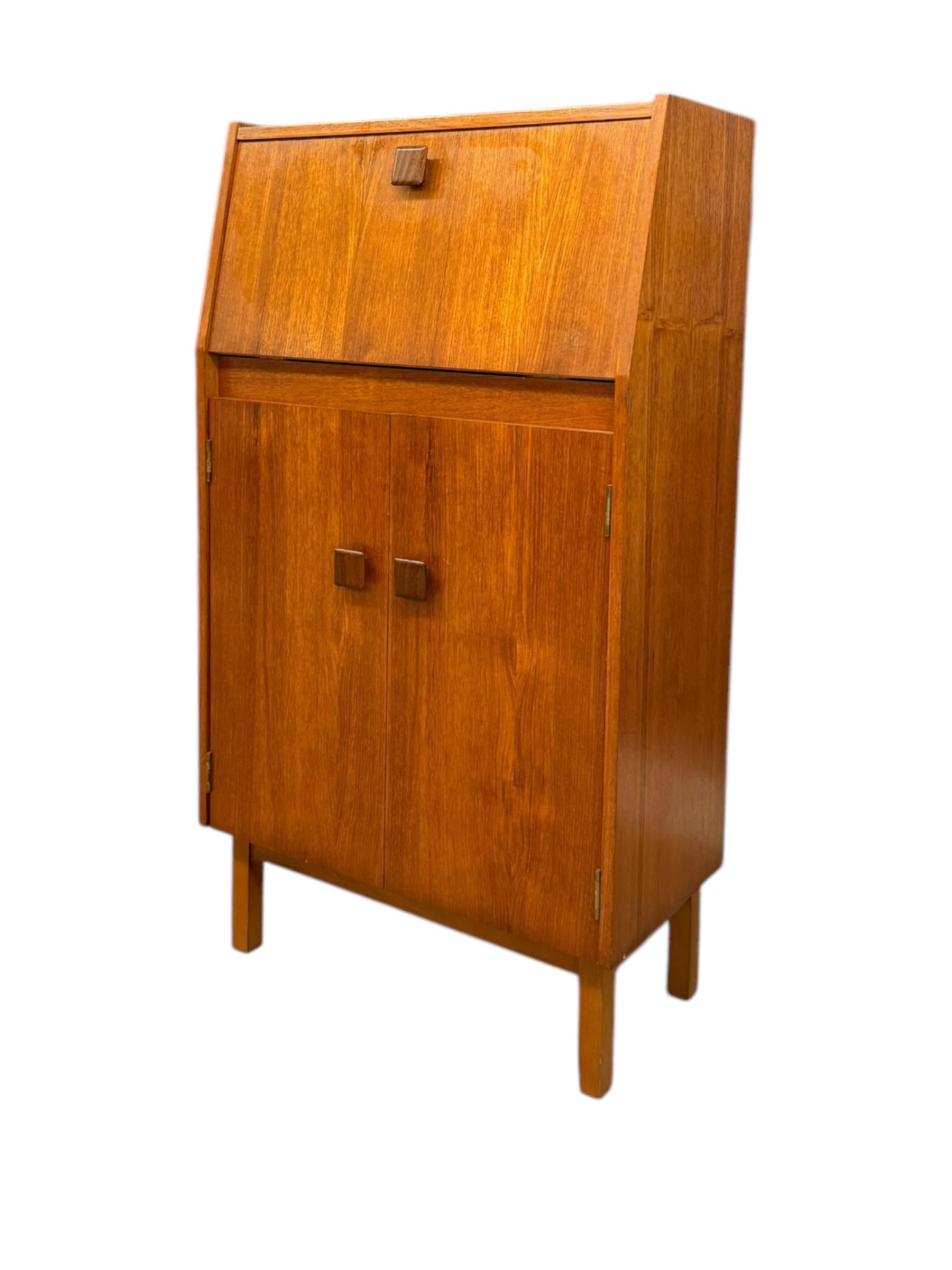 This Vintage Mid-Century Modern Teak Wood Petite Flip-Top Cocktail Table Bar Cabinet, likely an import from the UK, is a striking example of the era’s fusion of functionality and sophisticated design. Crafted from rich teak wood, the cabinet