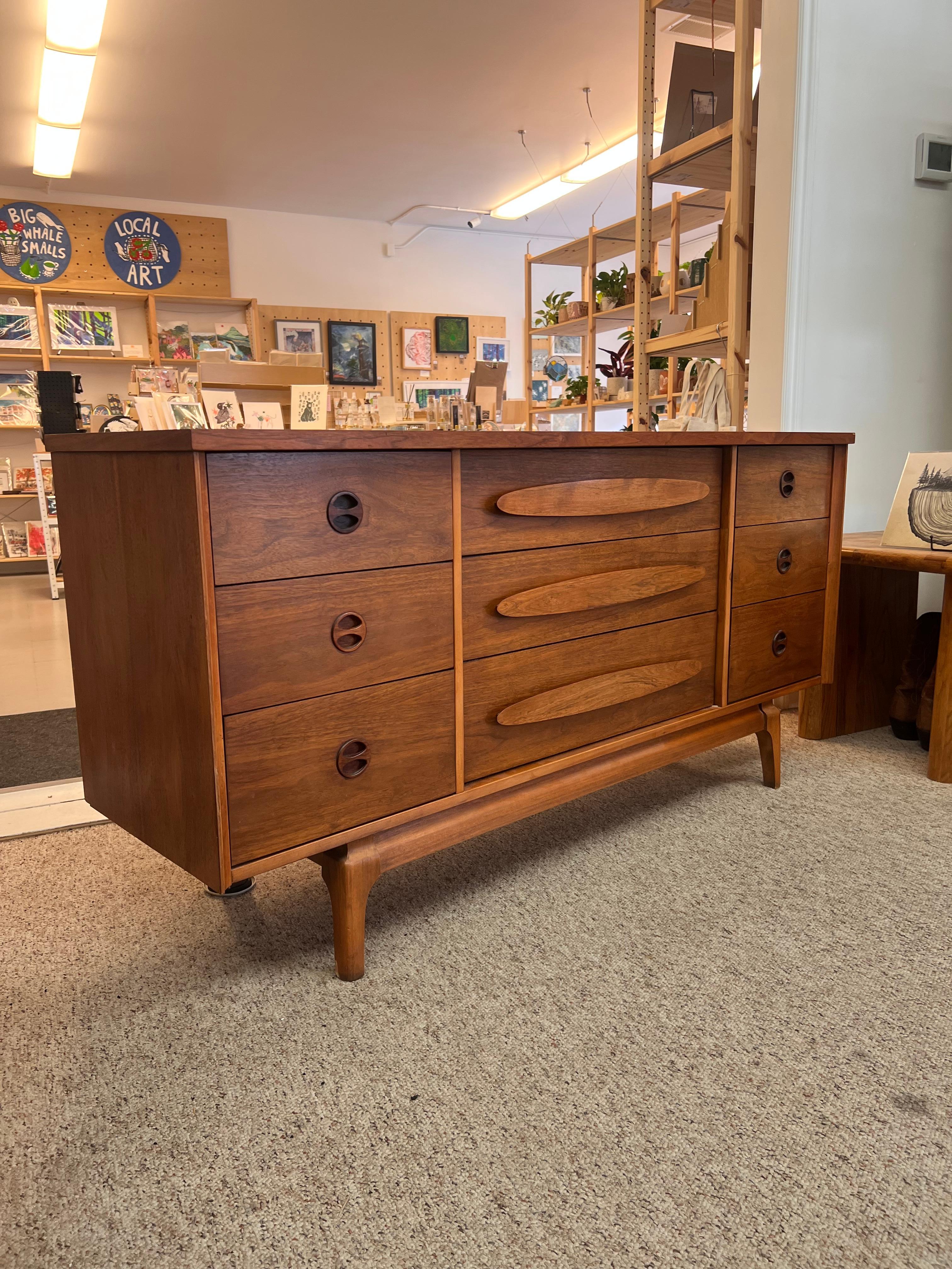 Commode basse vintage du milieu du siècle dernier en noyer avec neuf tiroirs, dont trois grands tiroirs au centre flanqués de six petits tiroirs sur les côtés. L'armoire repose sur une base à châssis et des pieds effilés. Les tiroirs sont montés en