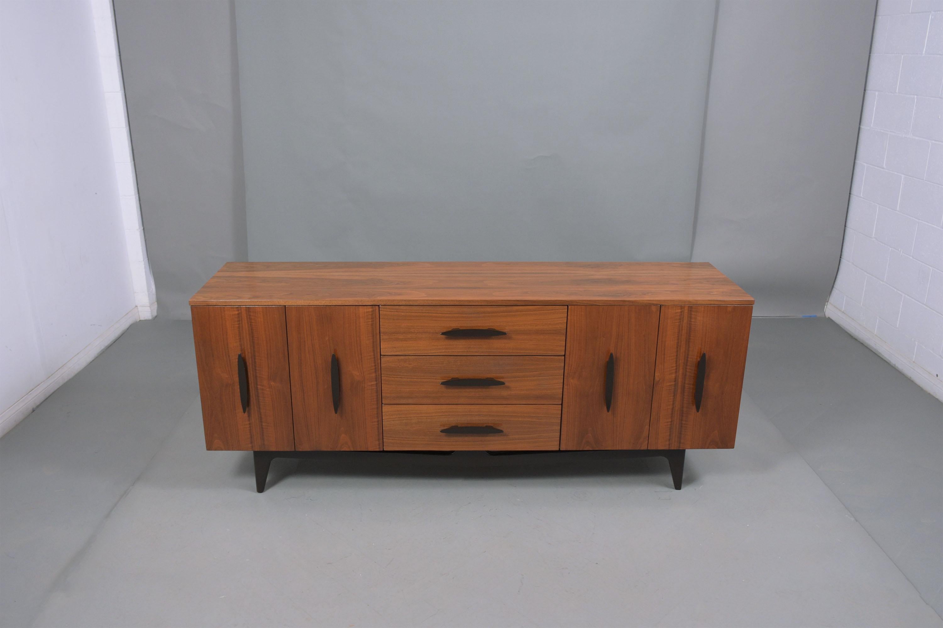 This 1960s mid-century walnut credenza is made out of walnut wood that has been stained in a walnut & ebonized color combination with a newly lacquered finish and fully restored by our craftsmen. The chest of drawers has three drawers down the