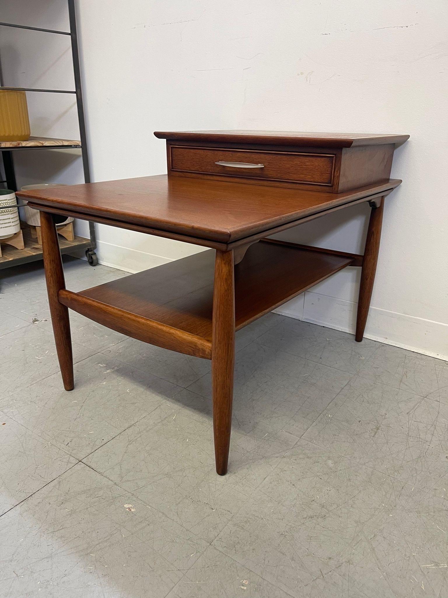 Walnut toned End Table with beautiful edge banding, dovetailed drawer, and tapered legs. Single drawer above open shelving. Makers mark located inside the drawer. Vintage Condition Consistent with Age as Pictured.

Dimensions. 29 W ; 21 D ; 23 H
