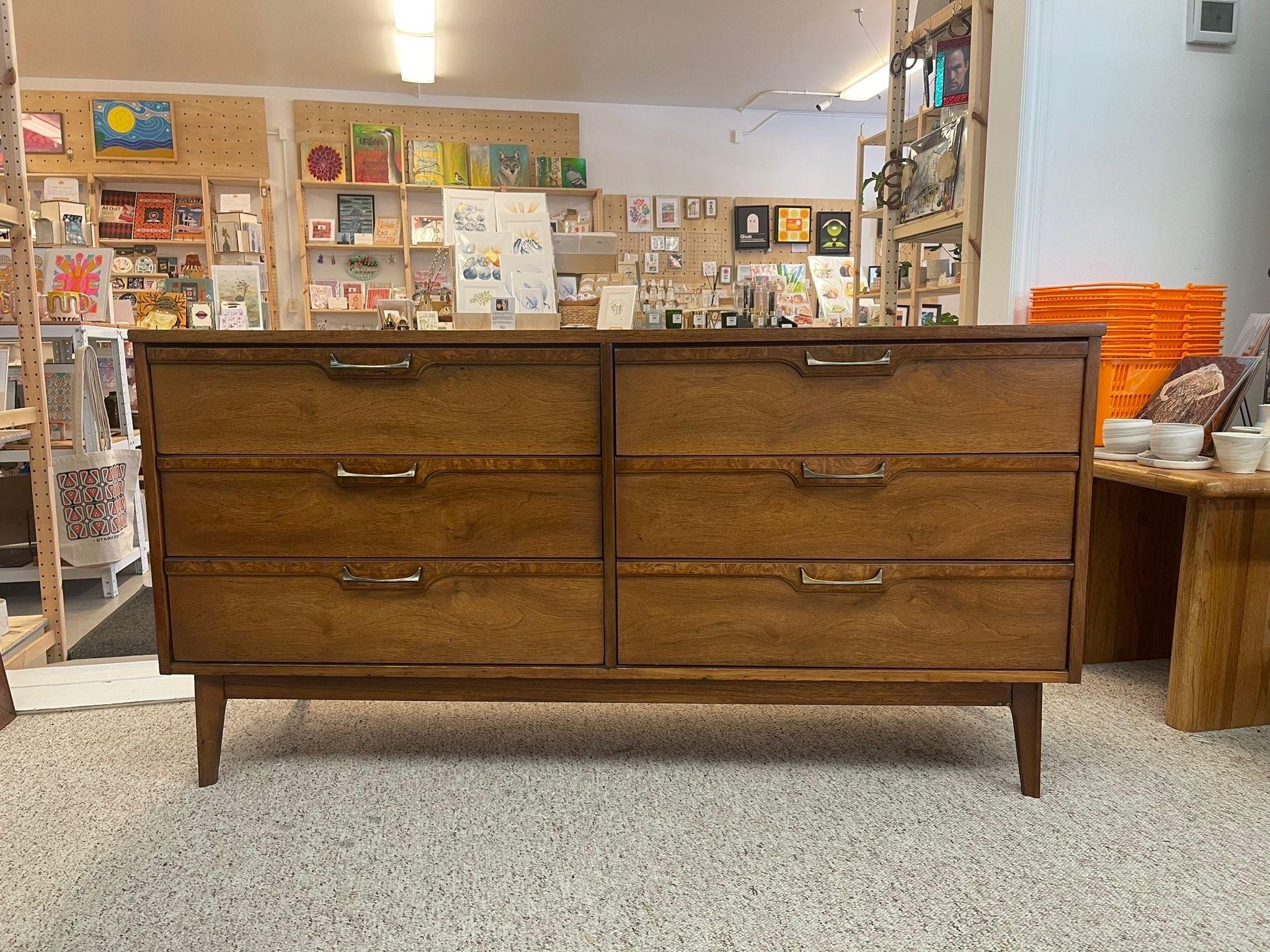 Walnut Toned six drawer dresser features Brass toned angled pulls accenting Burl wood highlights across the top of each drawer. Classic Tapered Legs and dovetailed drawers. Vintage Condition Consistent with Age as Pictured.

Dimensions. 60 W ; 18 D