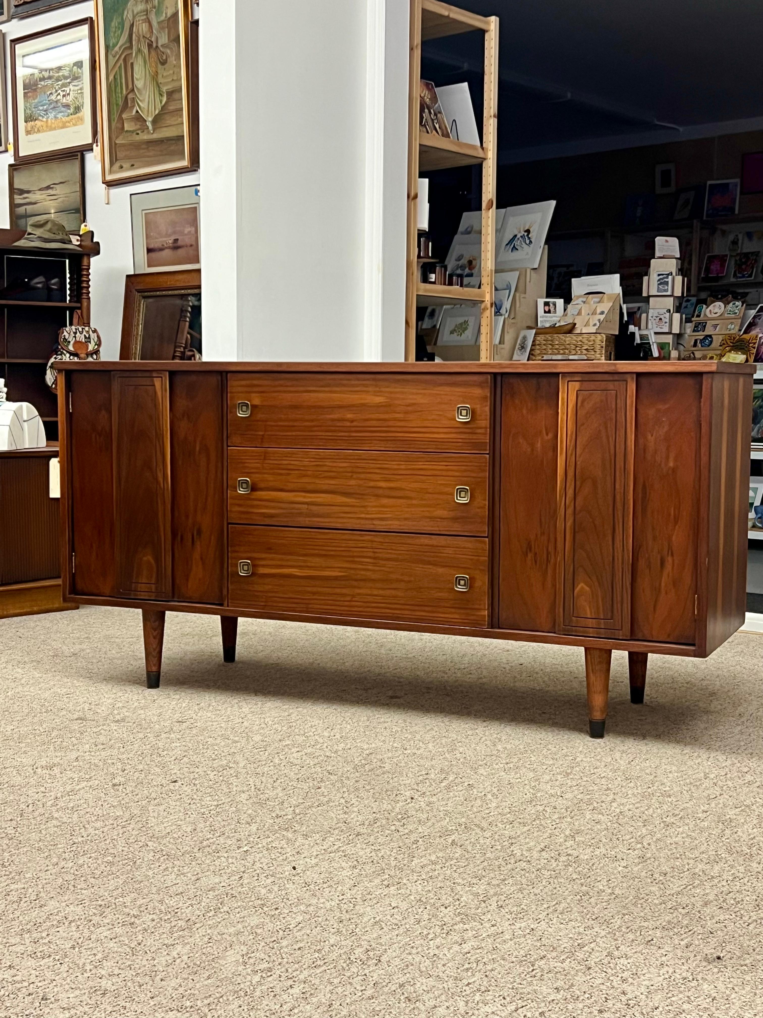 Wonderful vintage modern walnut credenza/ buffet by Stanley Furniture with three hefty drawers in the center and two large compartments on each side hidden by cabinet doors. The compact design offers plenty of room for storage without sacrificing