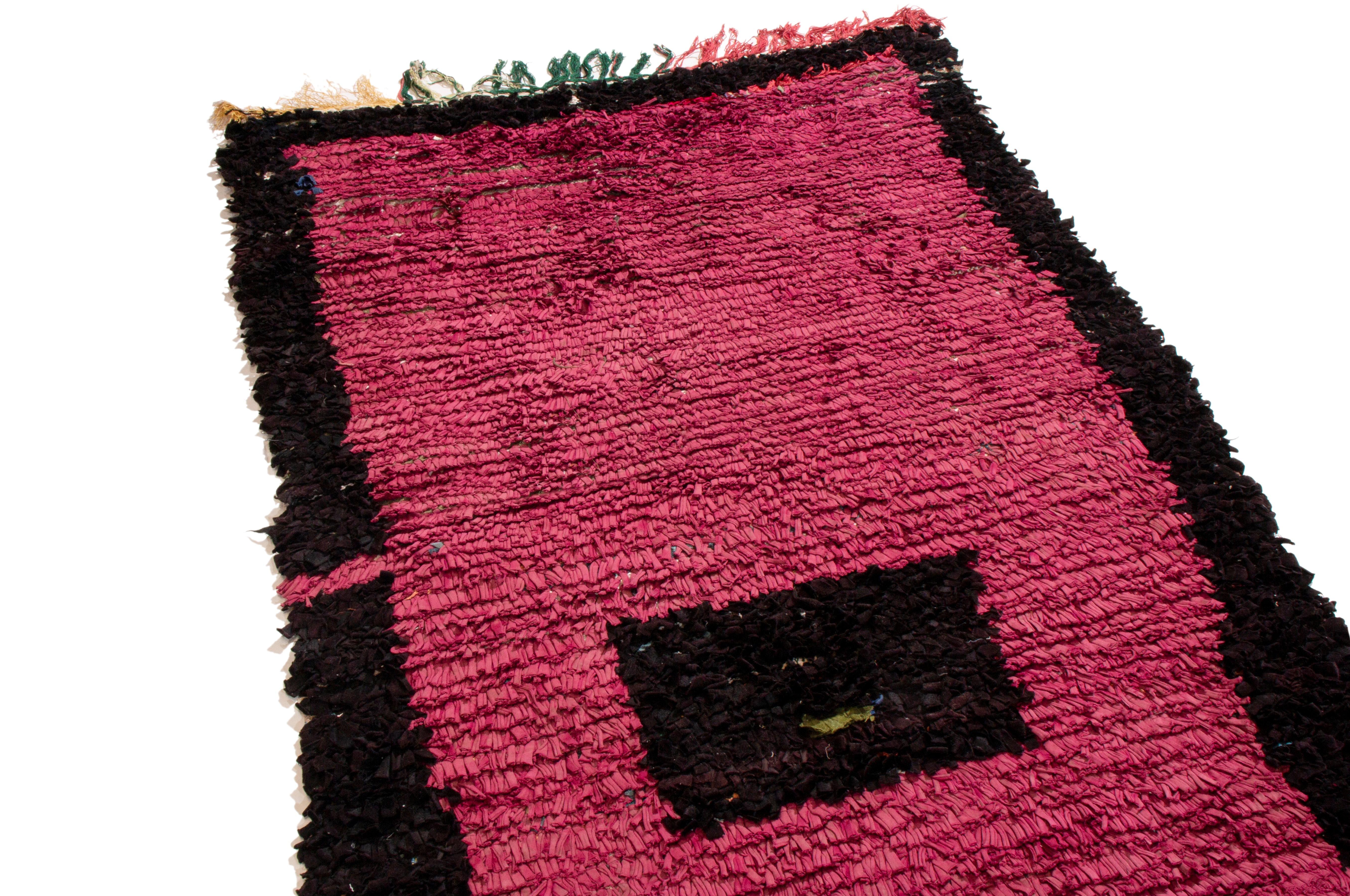 Originating from Moroccan in 1950, this vintage mid-century Moroccan wool rug features and uncommonly Minimalist transitional design with unique colorways. Hand knotted in durable textural wool pile, the combination of magenta and black colorways