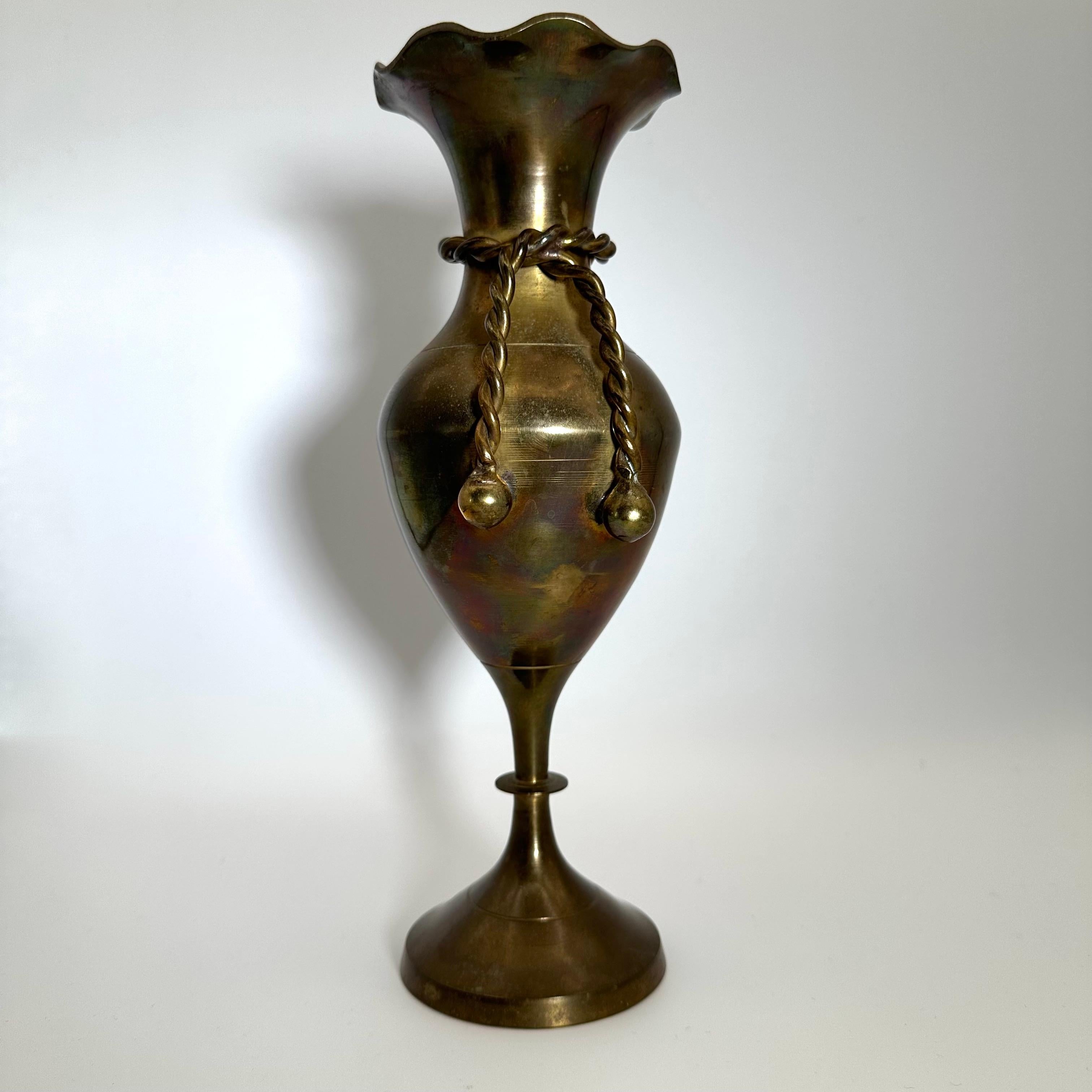 A beautiful and shapely vase cast in brass with one of a kind patination, creating a multicolor appearance. Featuring a curvy, bulbous shape, ringed at the neck by a twisted braided rope, terminating with ball or bead motifs on the ends. Opens at