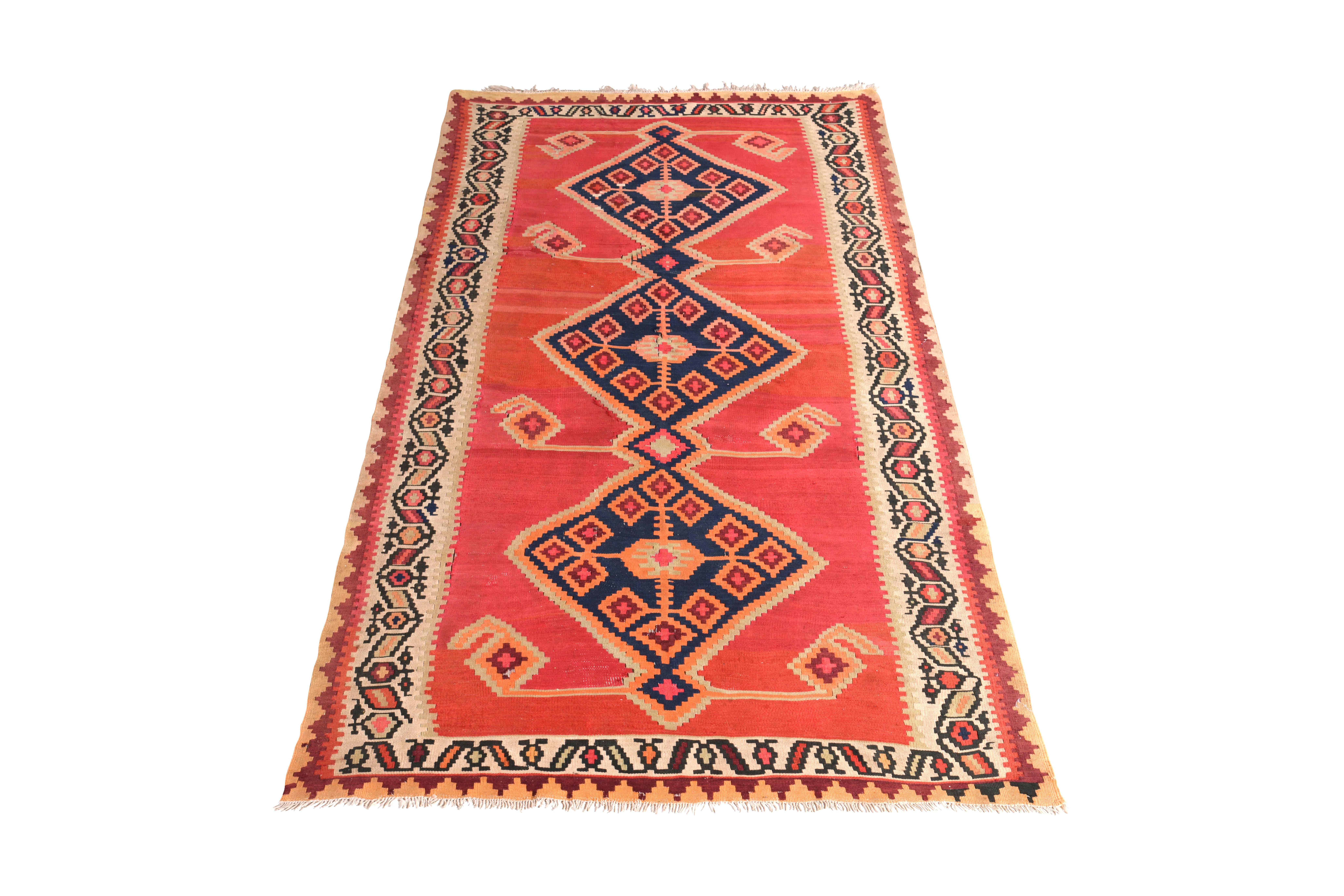 Handmade in flat-woven wool circa 1950-1960, this vintage rug is a midcentury Persian Kilim in a notably warm red colorway, both complemented and counterbalanced with a navy blue and orange medallion field pattern and forgiving hues of beige in both