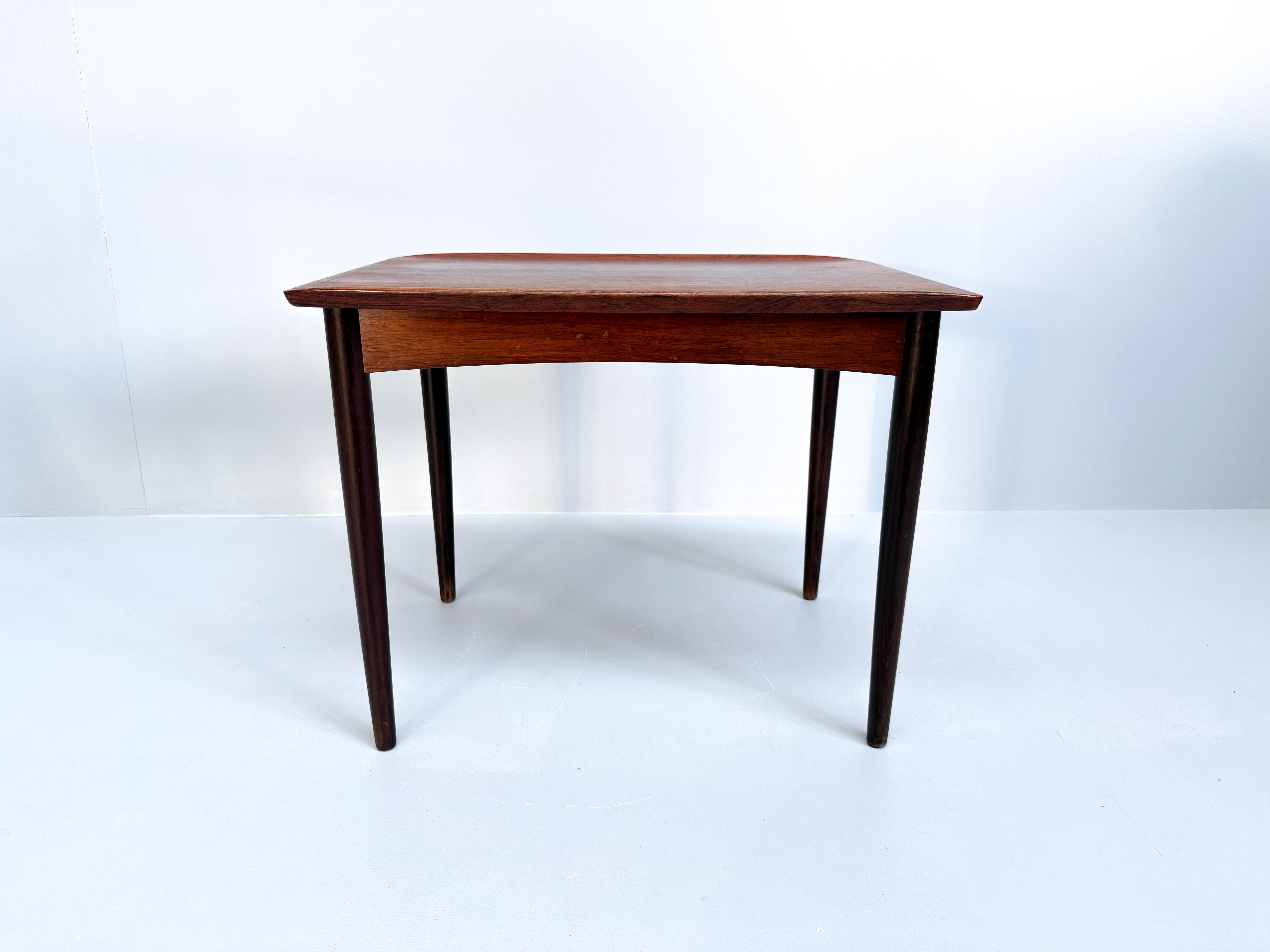 Preciosa mesa danesa vintage de mediados de siglo hecha de palisandro. Tiene una parte superior rectangular con bordes suavemente curvados y una superficie lisa y pulida. La mesa se apoya en cuatro patas esbeltas y cónicas que se inclinan