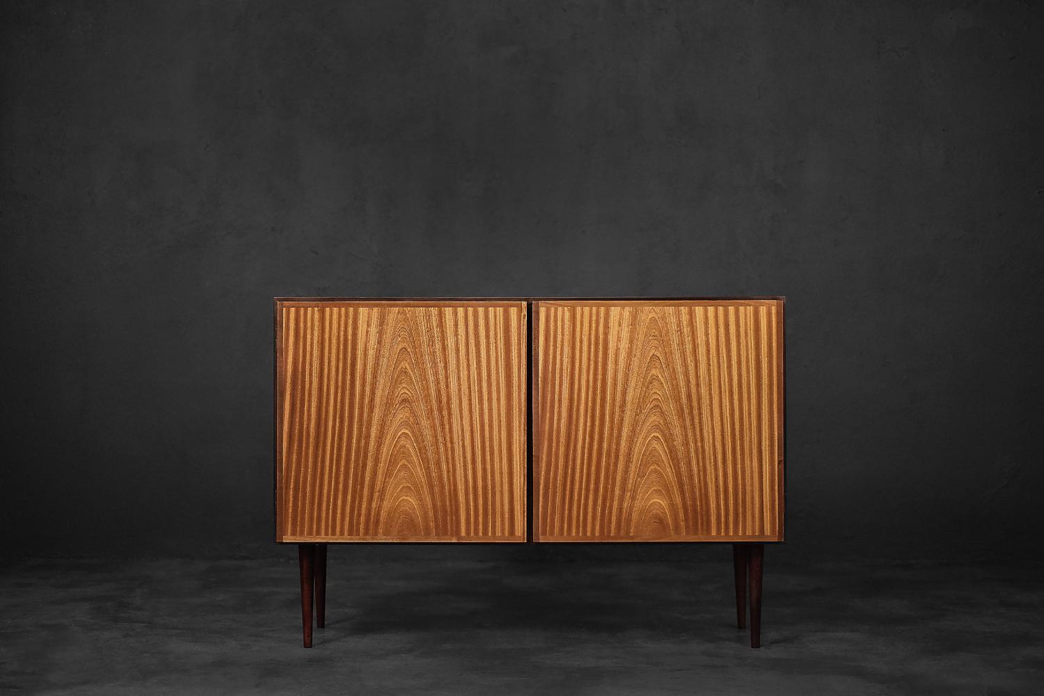 This cabinet was designed by Gunni Omann for the Danish manufacturer Omann Jun Møbelfabrik during the 1960s. It is model number 4. The two-door cabinet is made of beautiful and rare mahogany wood in a honey shade of brown. The wood grain is clear,