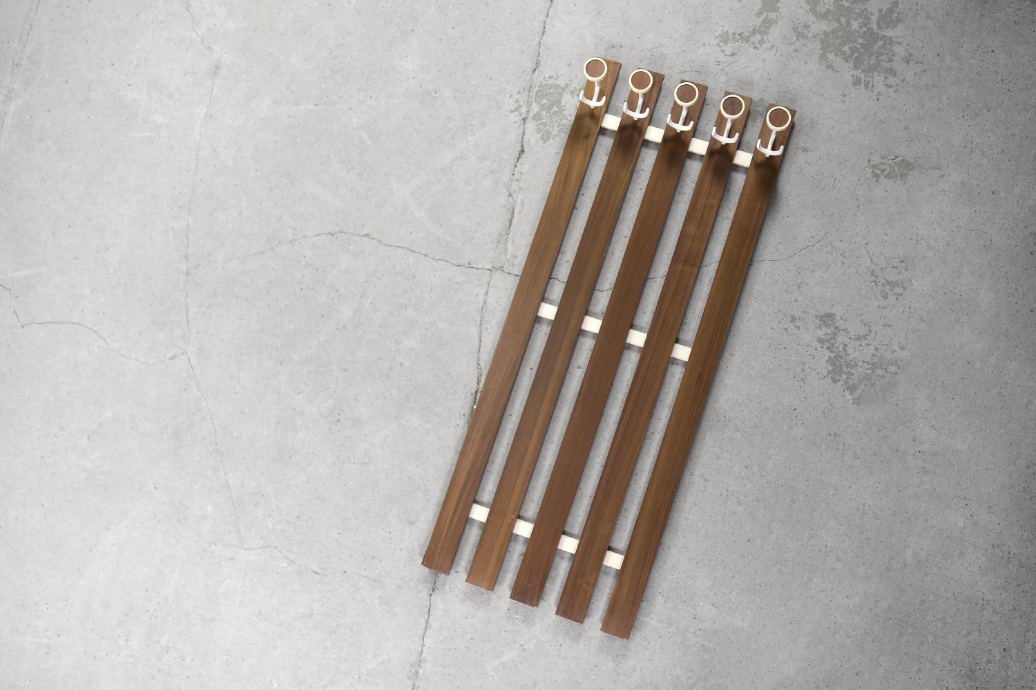 This modernist coat rack was made in Denmark during the 1950s. It was finished with teak wood in a warm shade of brown. It has five double clothes holders, which are made of metal in white colour and are finished with a geometric shape in plastic.
