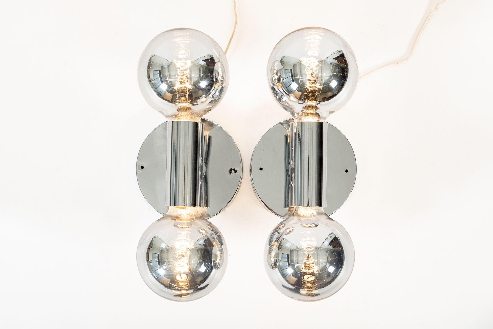 This pair of large, vintage mid century modern silver chrome wall sconce lights by Robert Sonneman are circa 1970. The unique, minimalist design features a simple, center cylinder tube with a 5” silver-coated bulb on each end mounted on a round