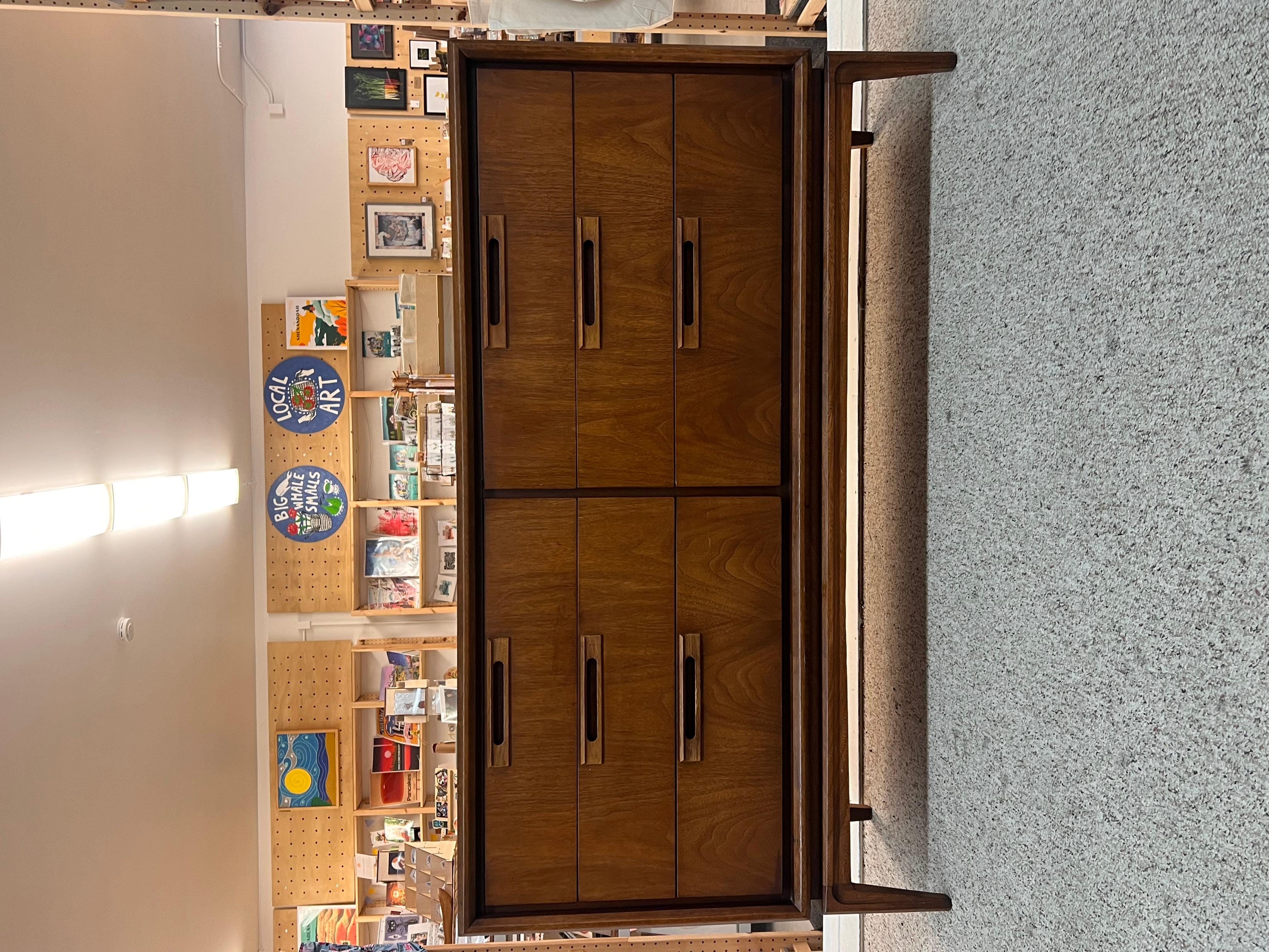 This United mid-century modern 6-drawer dresser features a sleek and elegant design typical of the era. The dresser is constructed from rich, warm wood, showcasing the natural grain that adds character and charm. It has six spacious drawers,