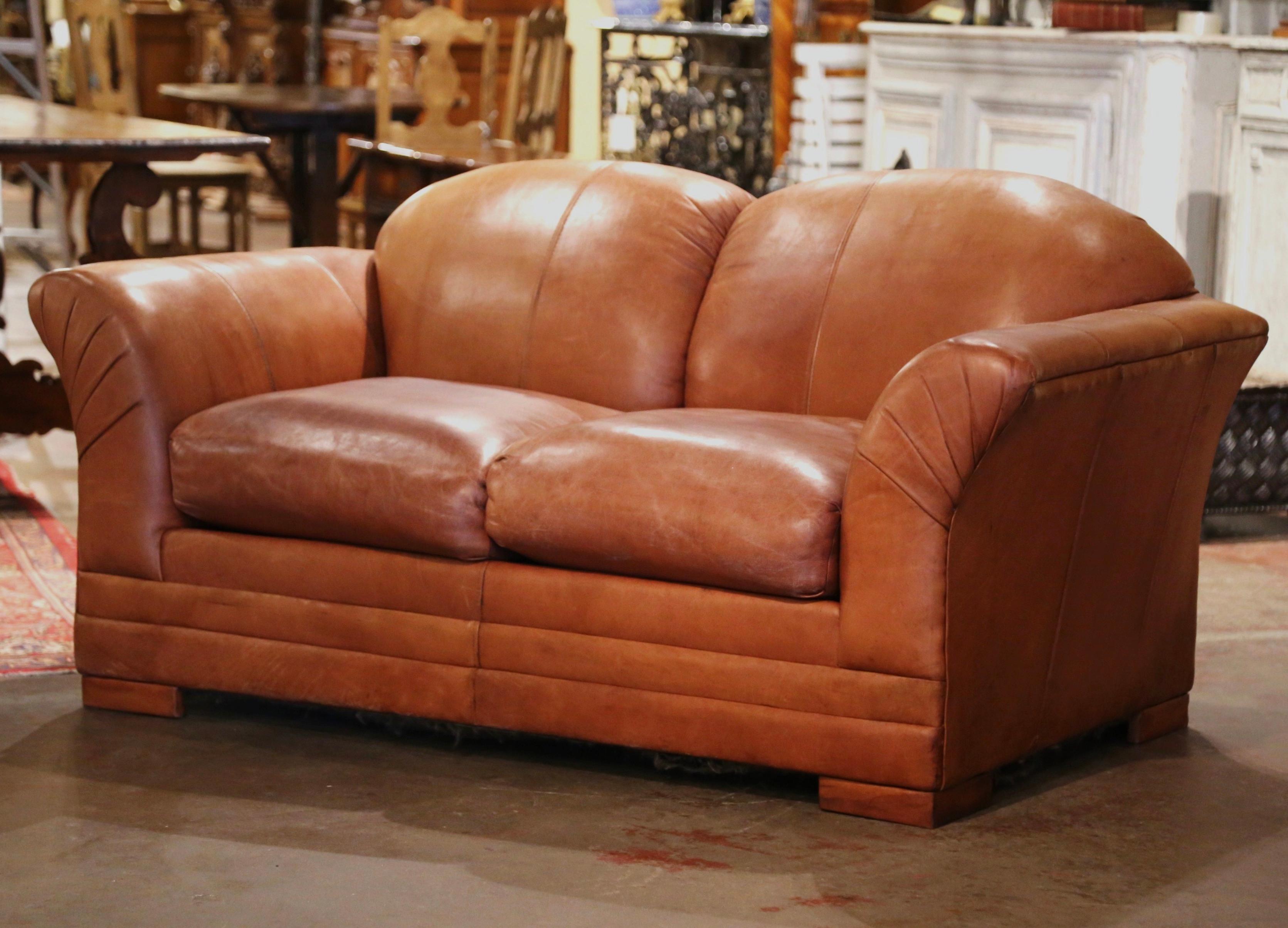 This Classic, antique Art Deco club sofa was crafted in France, circa 1950. This stately couch features wide, rounded armrests, a pitch back with an arched top shape, and square feet covered with leather at the base. The Classic, masculine French