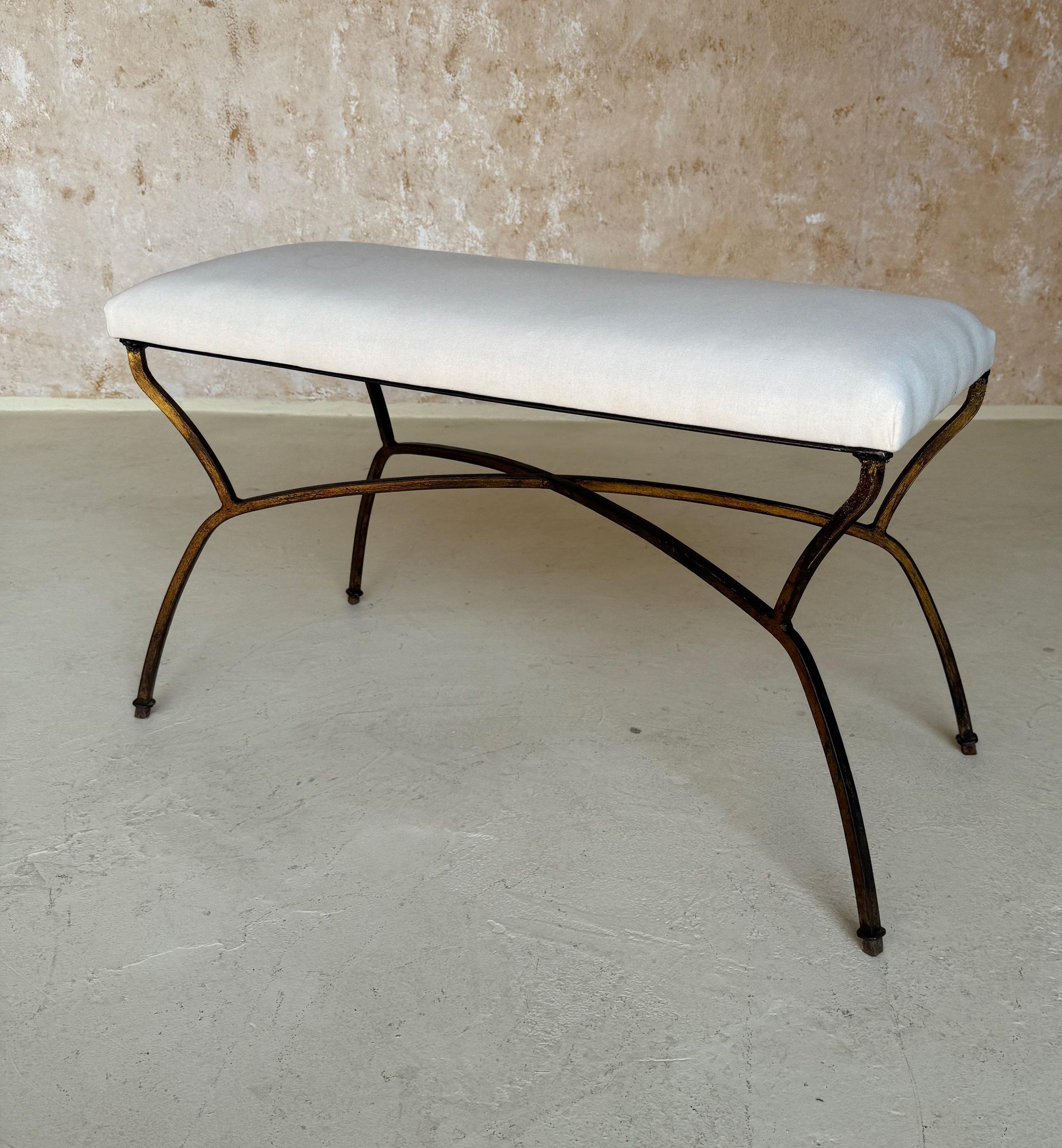 This elegant mid century Spanish gilt iron bench was crafted by skilled artisans and features a hand forged base with gracefully curved legs and an arched double stretcher that criss crosses in the middle. The rich gold gilt finish is hand applied.