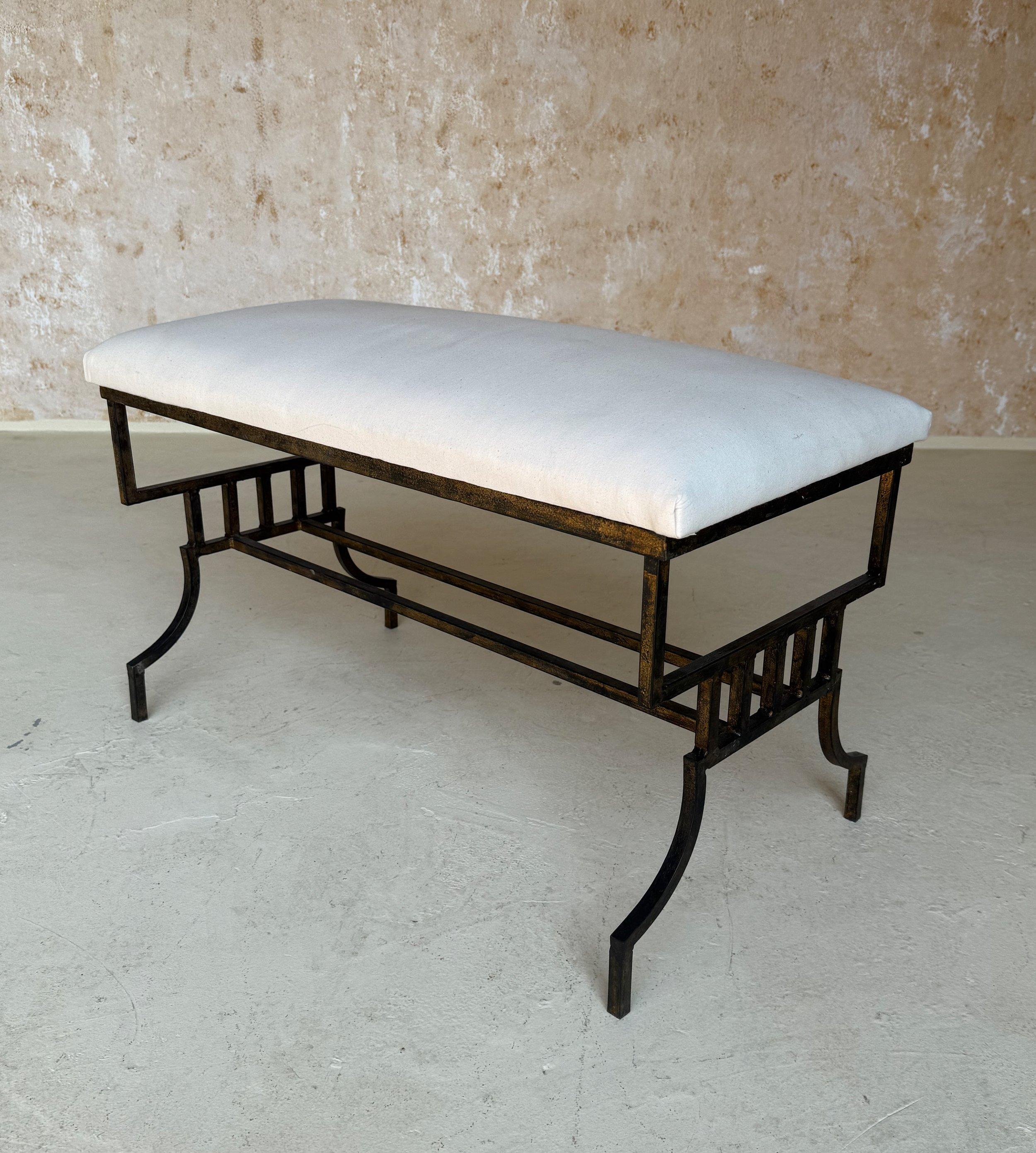 This magnificent vintage mid century modern Spanish iron bench from the 1950s features a hand forged geometric frame with a double stretcher. The rich, dark patina with traces of gold is original to the piece. The seat is finished in muslin, ready