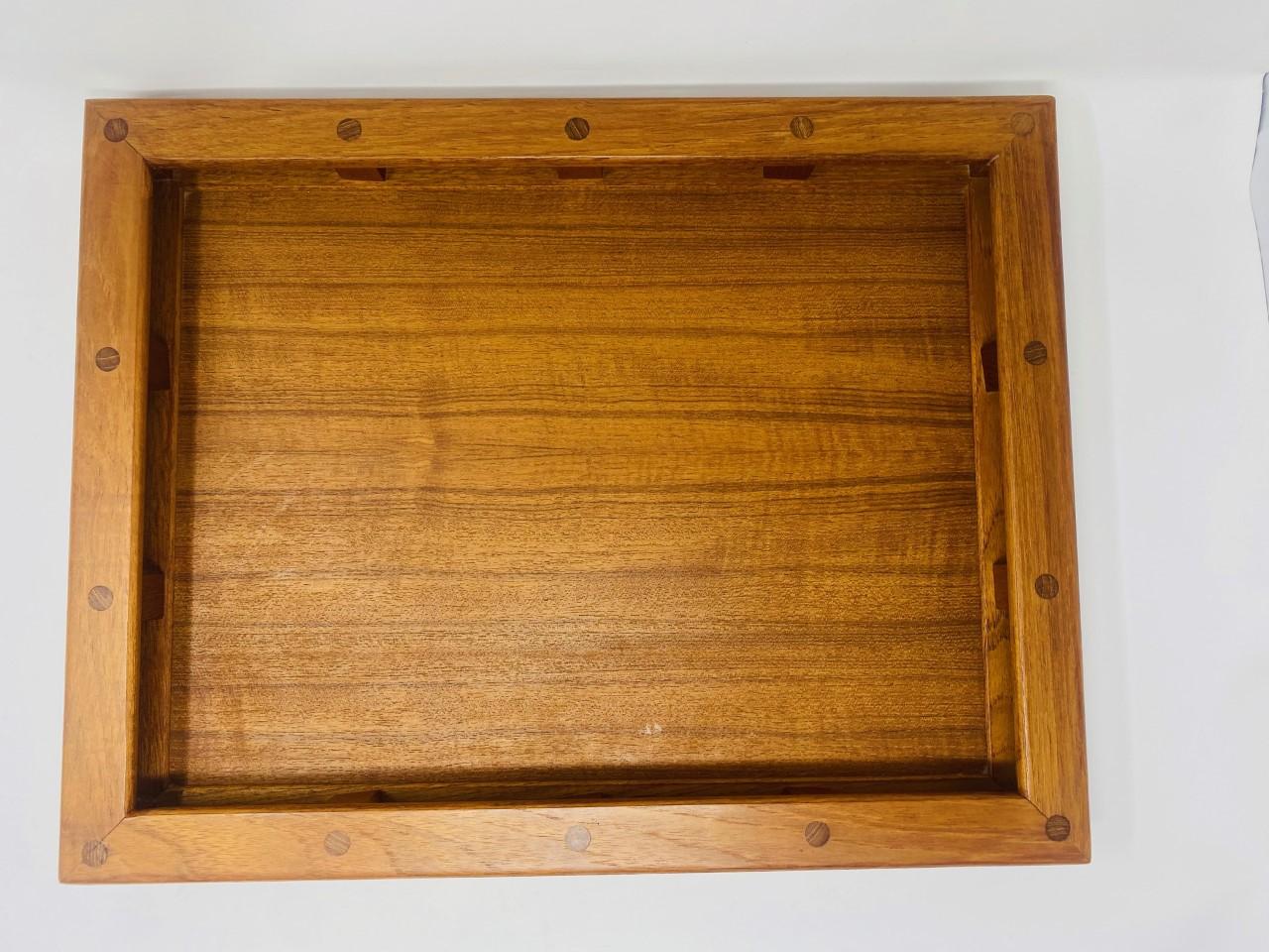 Beautiful serving tray in teak by Dansk. This piece is well crafted in solid teak wood and built in rail styled handles. The piece has pegged detail construction that finishes a beautiful look. Branded mark to the verso manufactured by Dansk IHQ