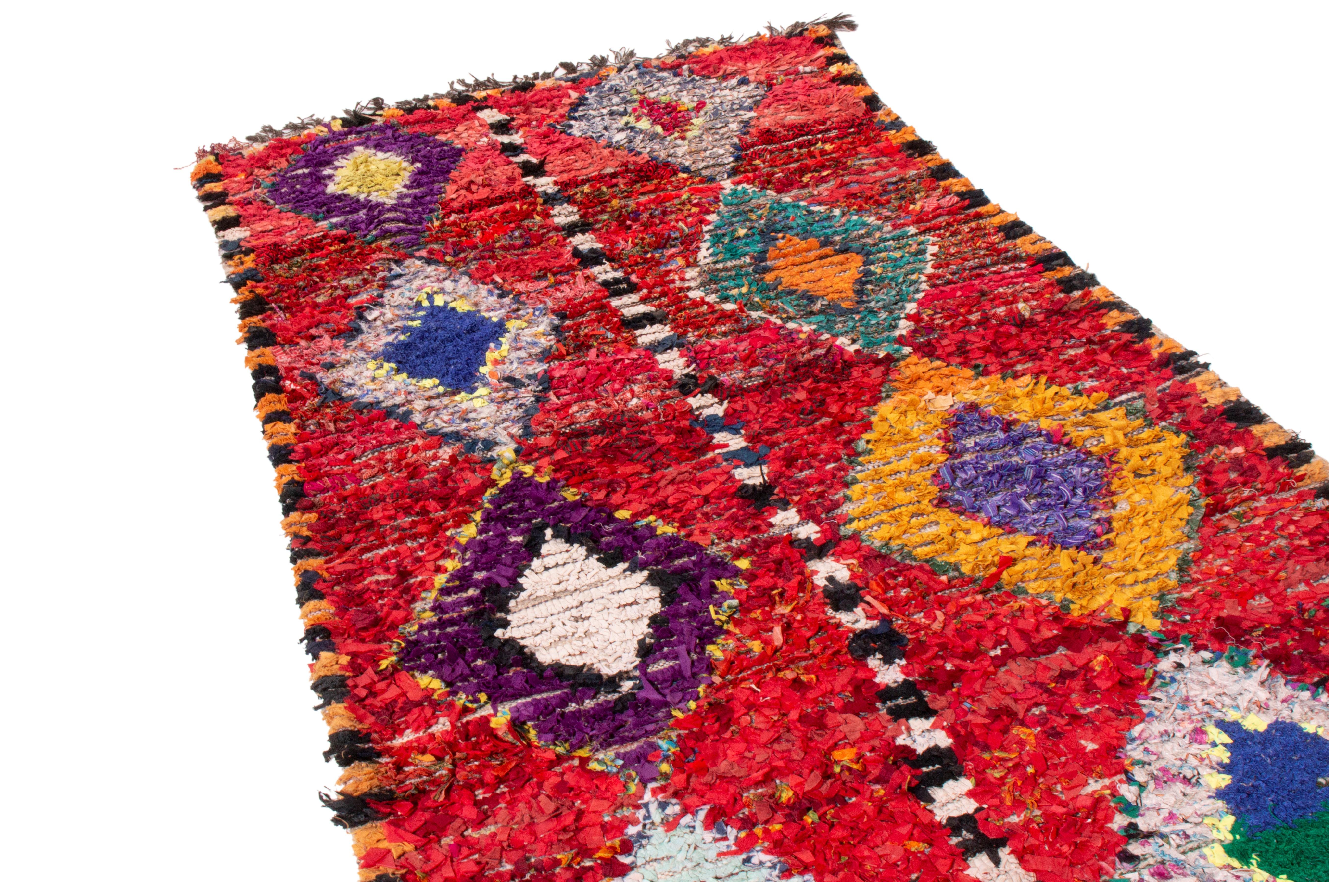 Originating from Morocco in 1950, this vintage mid-century transitional Moroccan rug employs a distinct geometric orientation to its culturally significant symbolism. Hand knotted in high quality wool pile, the textural, plush blood red field with