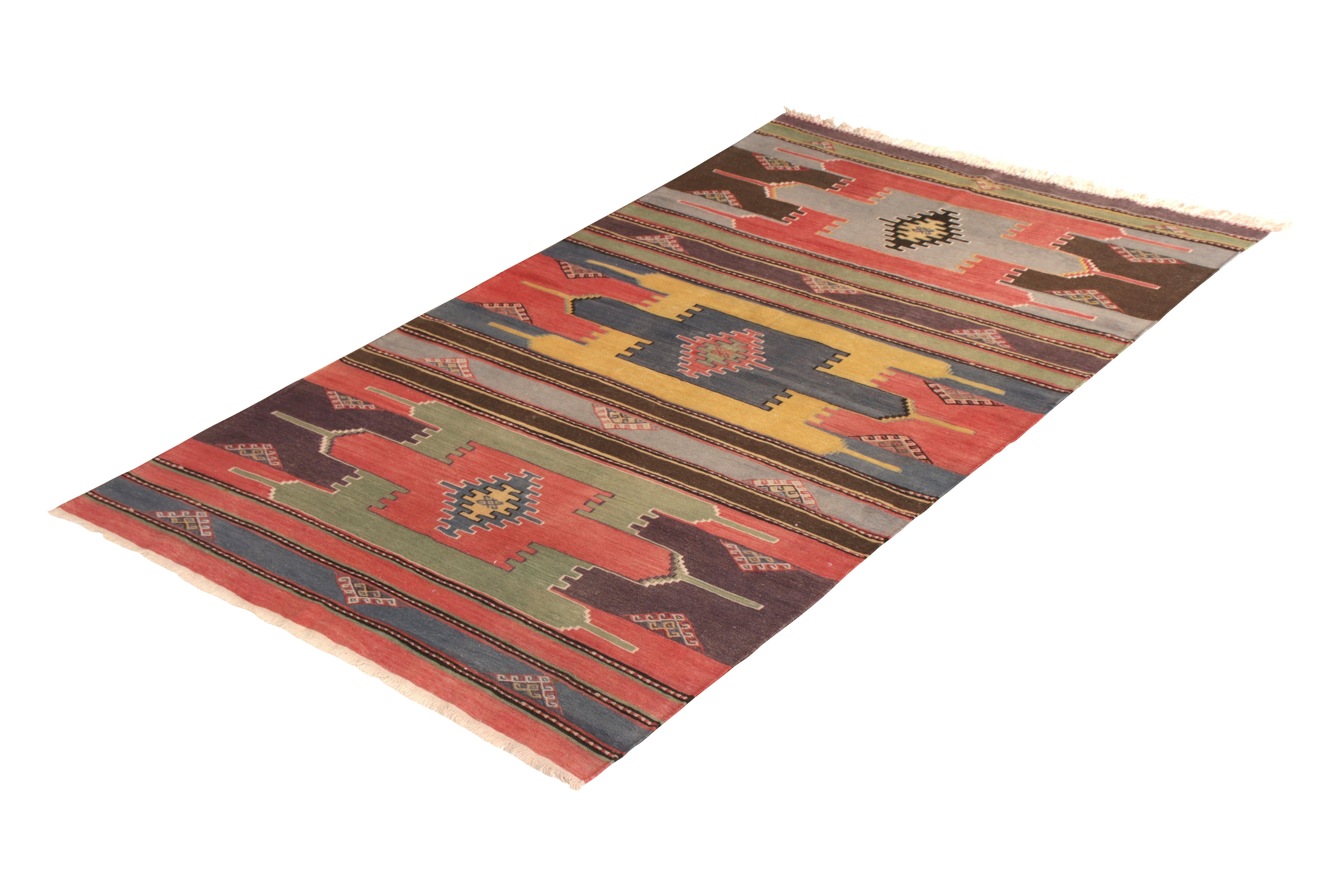 Handmade in flat-woven wool originating from Turkey circa 1950-160, this midcentury rug is a vintage Kilim of notable tribal nature, employing both an arresting geometric all-over pattern and a series of exciting blue, red, green, and yellow