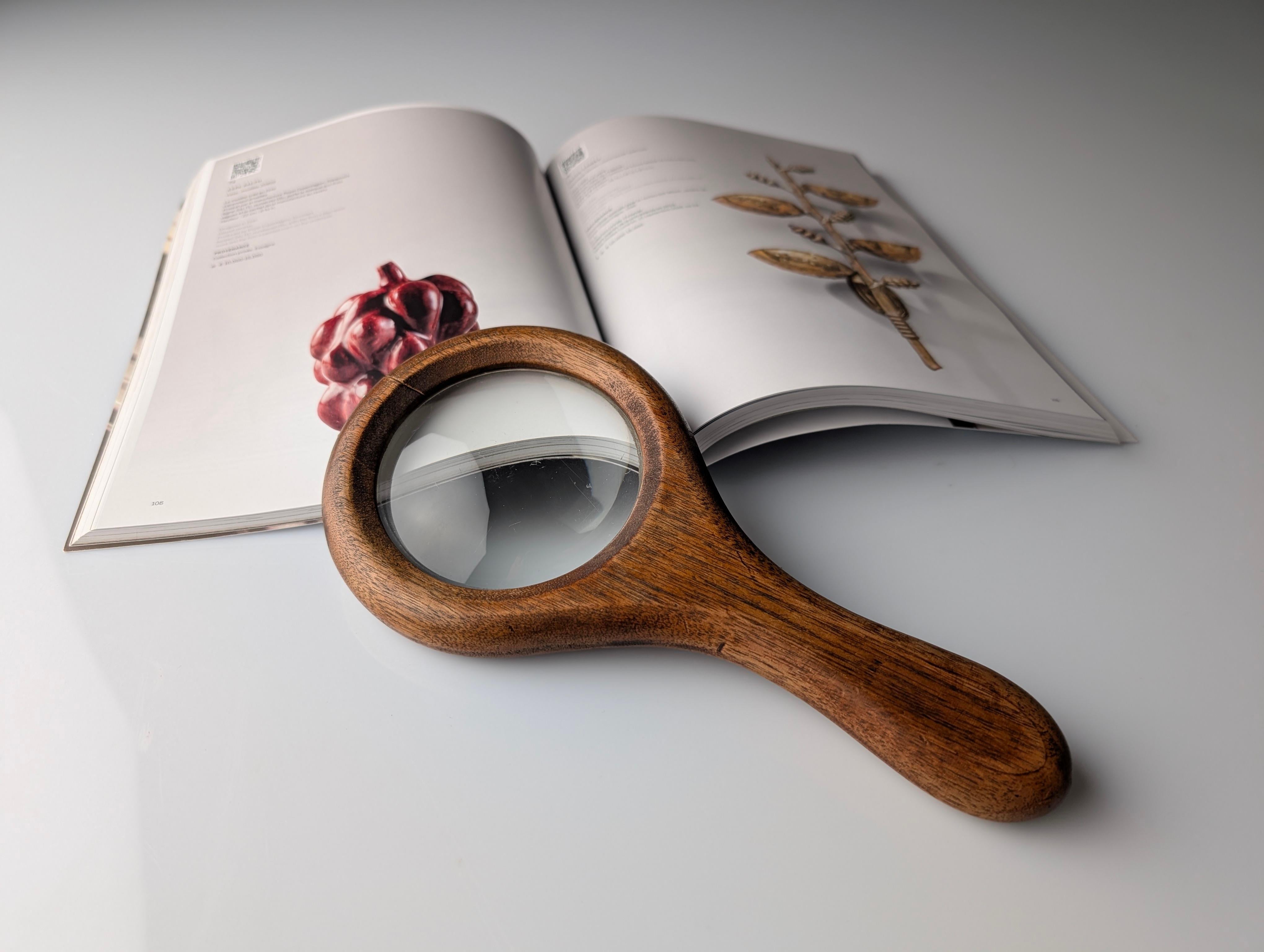 Questo oggetto è una lente d'ingrandimento elegantemente semplice risalente al periodo di metà secolo, probabilmente prodotta in Italia intorno agli anni Cinquanta o Sessanta. Il pezzo si distingue per la forma organica e morbida del manico e della