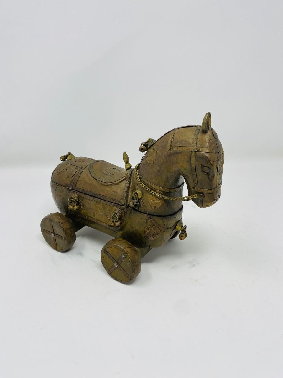 Vintage Sudha Pennathur brass covered wooden trojan horse. This horse figure has been handmade in India by Sudha Pennathur (Designer). This horse figure has a primitive style and is ornately covered with brass details, emblems and bells. The body of