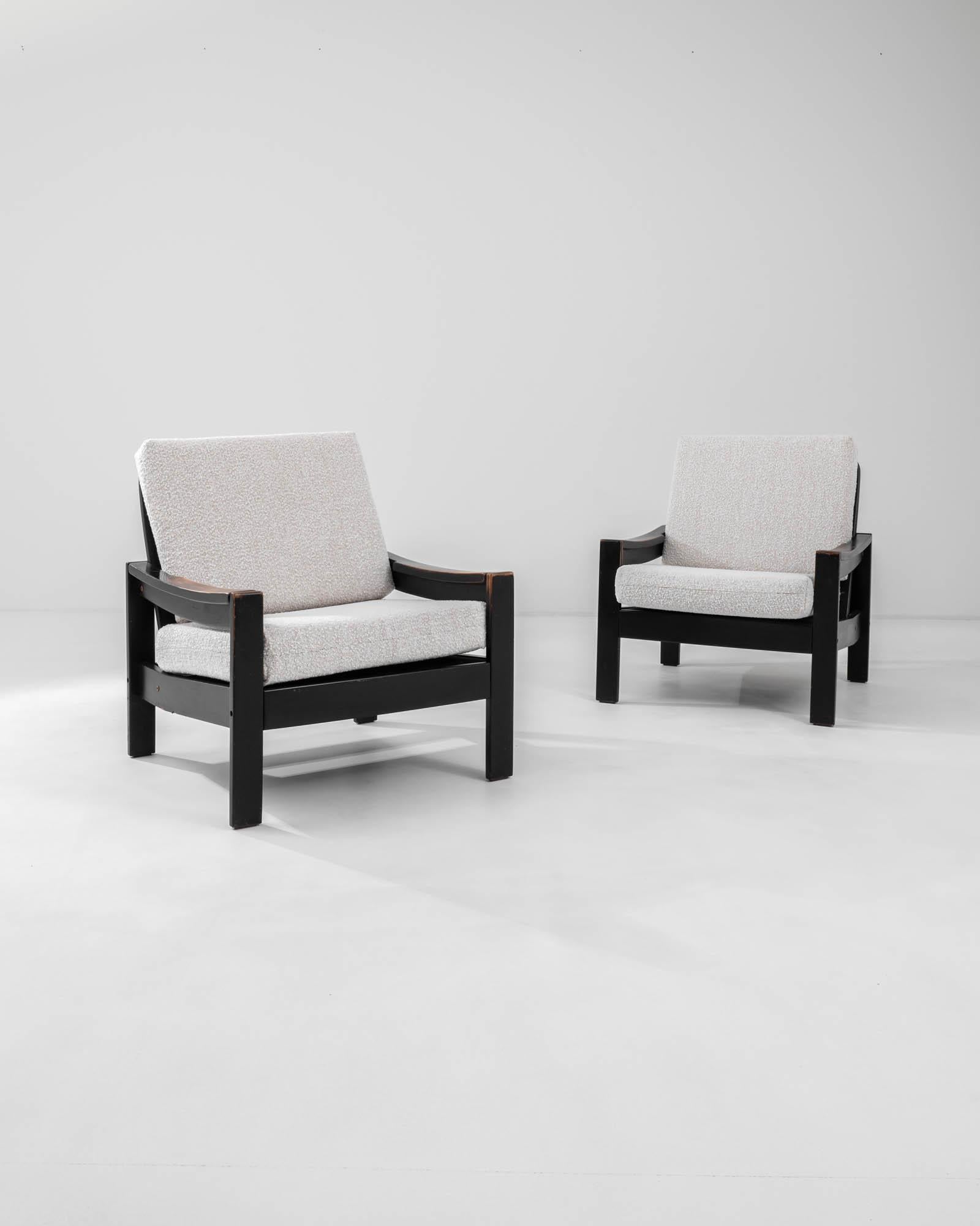 A pair of wooden upholstered armchairs created in 20th century Europe. With a dignified yet relaxed posture, these sumptuous chairs invite one to recline in distinguished style. Created in a classic mid-century design, these chairs exude a cozy yet