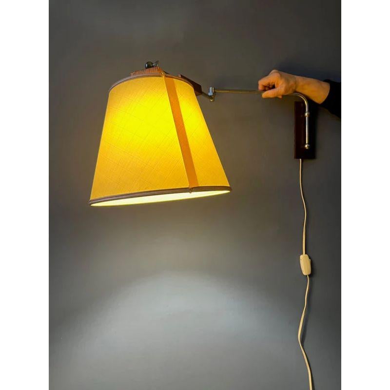 Classy mid-century wall lamp with textile shade and wooden elements. The lamp has a beige textile shade and the arm consists of metal and wood. The lamp requires an E27 (standard) lightbulb and currently has an EU-plug.

Dimensions:
ø Shade: 28