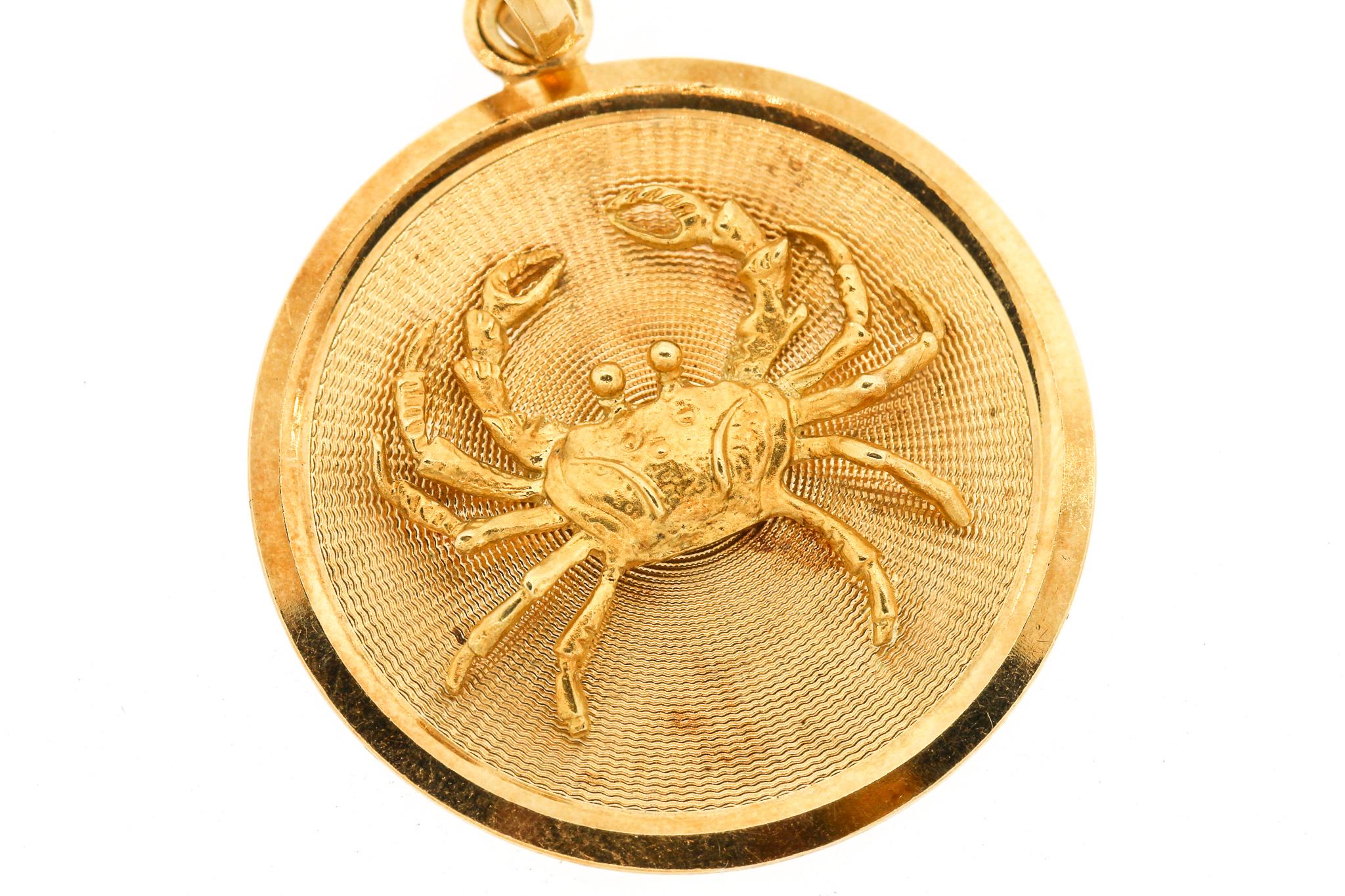 A round 18k gold mid-century Zodiac Cancer disc charm or pendant. The charm depicts a dimensional crab in motion on the front of the charm. The crab is on a textured fluted gold background with a smooth frame around the charm. It is suspended by a