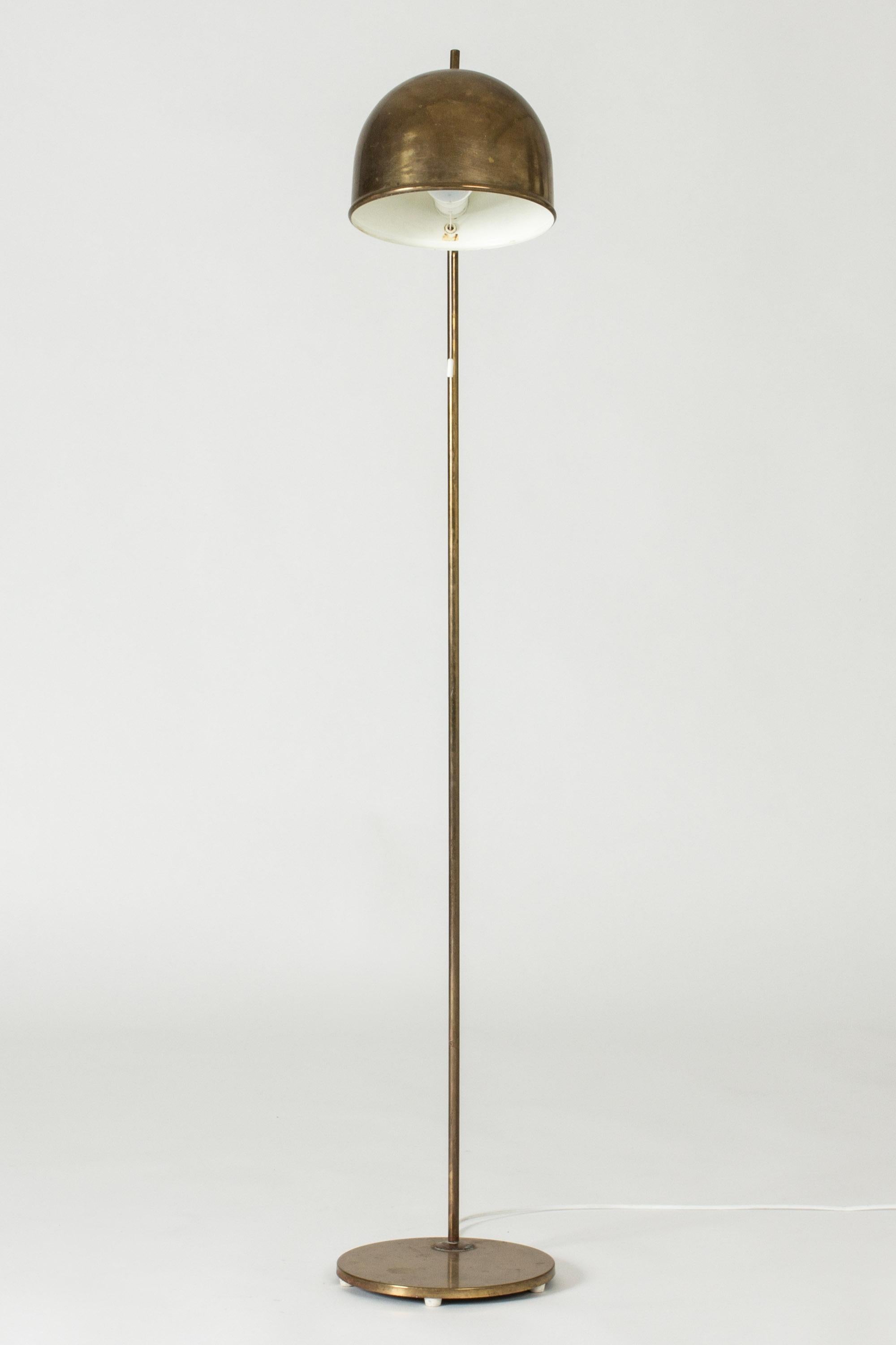 Brass floor lamp from Bergboms, with a sleek, rounded design topped off with a little tip at the top of the lampshade.