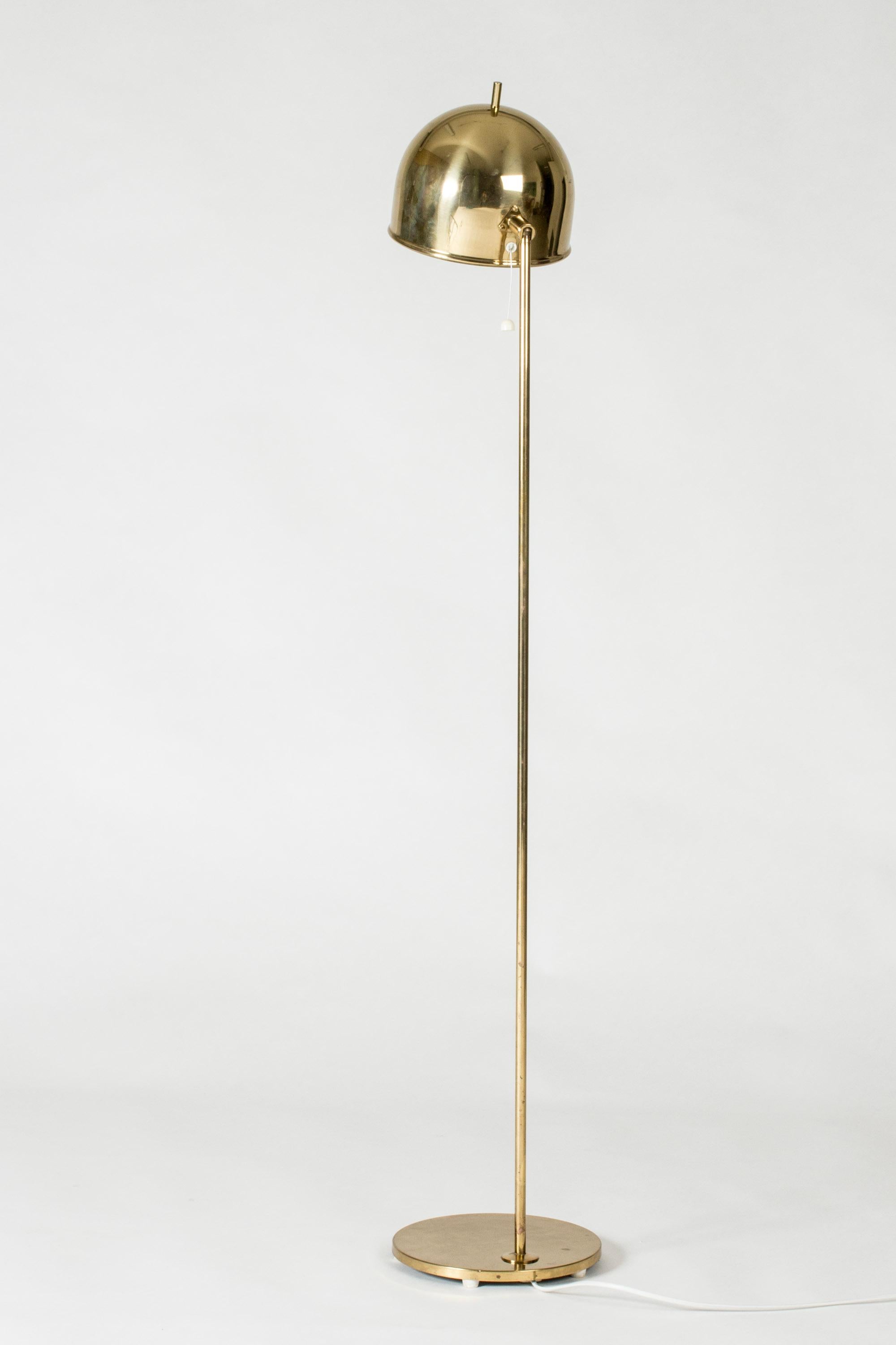 Brass floor lamp from Bergboms, with a sleek, rounded design topped off with a little tip at the top of the lampshade.