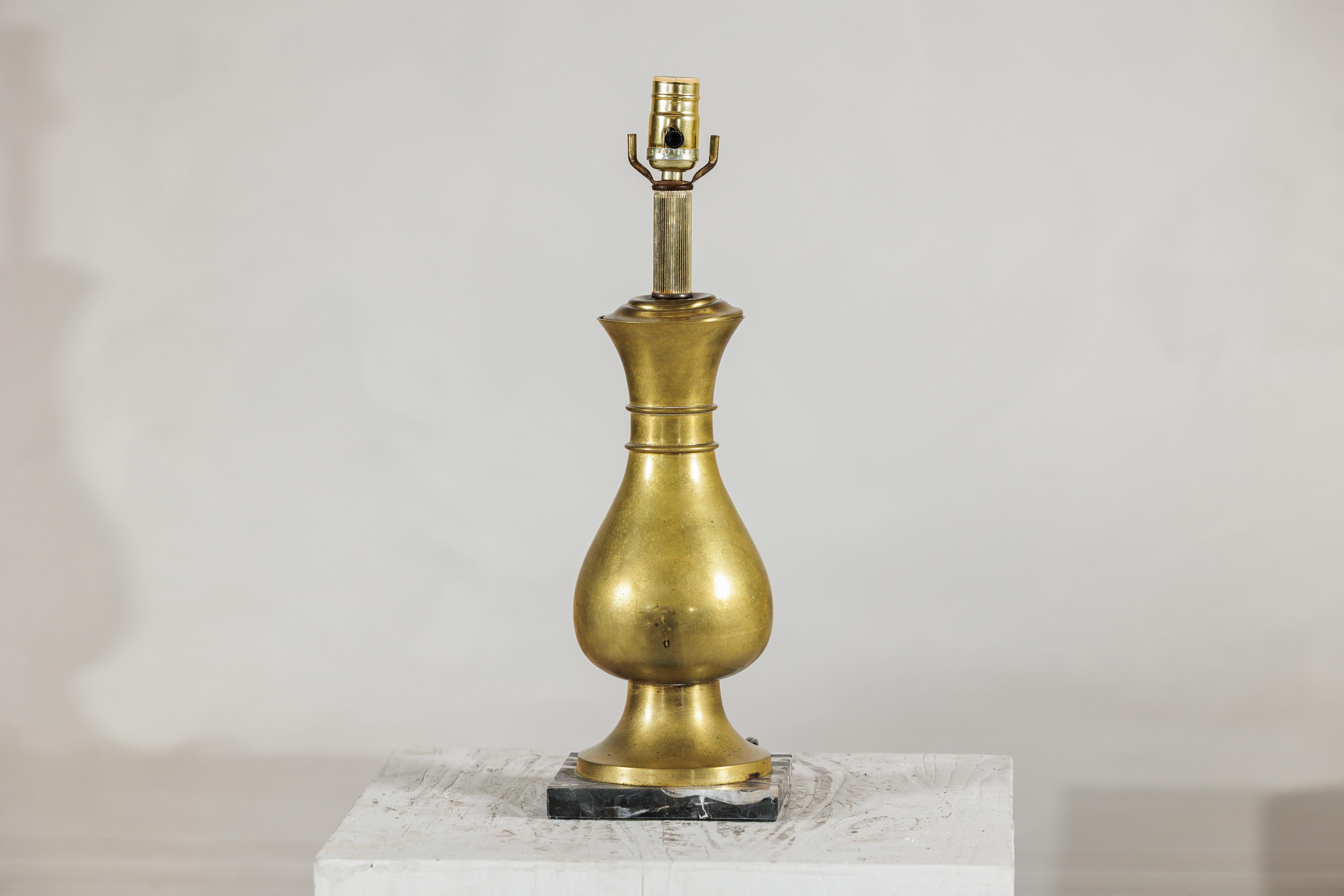 This vintage brass table lamp offers a classic mid-century presence, defined by its sculptural baluster silhouette and warm, naturally aged surface. The body is shaped with a gentle, elongated curve that narrows at the neck, accented by two subtle