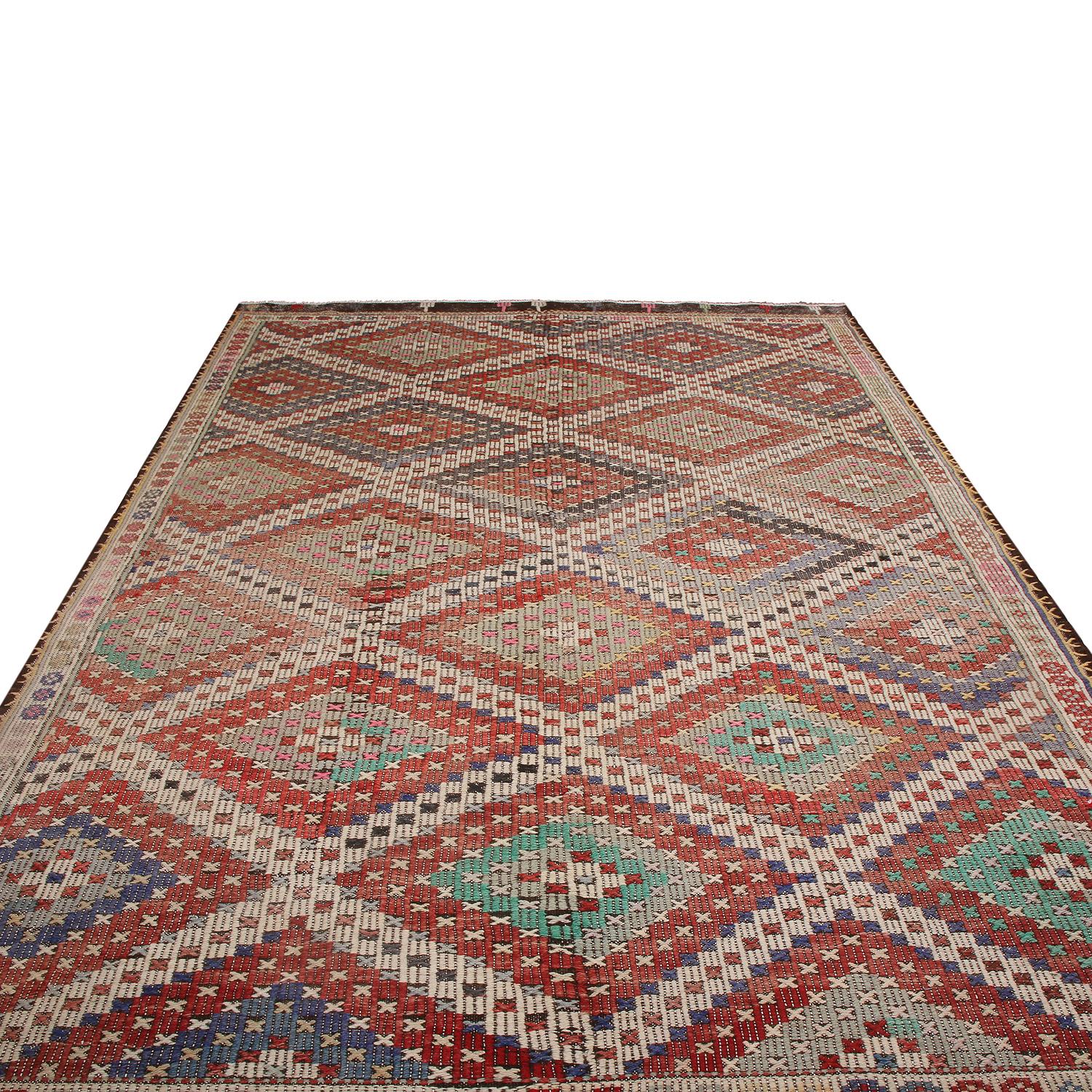 Flat-woven in Turkey originating between 1950-1960, this vintage midcentury Kilim hails from the city of Denizli, enjoying uniquely subtle variations in the accenting green, blue and pink hues among Turkish rugs playing tastefully off the rich red