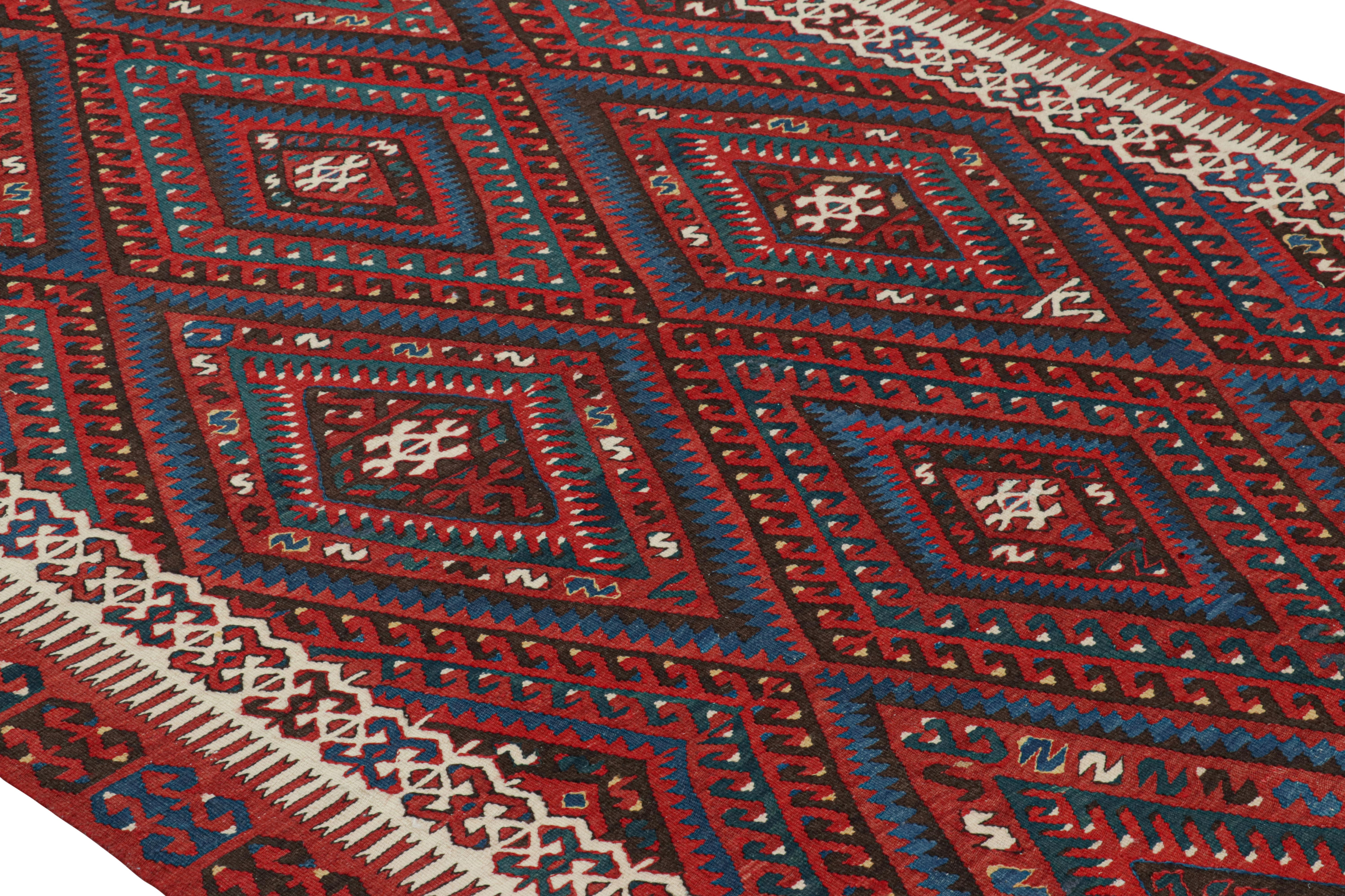 Flat-woven in Turkey originating between 1950-1960, this vintage midcentury Fethiye wool rug enjoys a classically appealing diamond field design, marrying a bold tribal pallet of burgundy red and blue with intricate accents of beige in the border