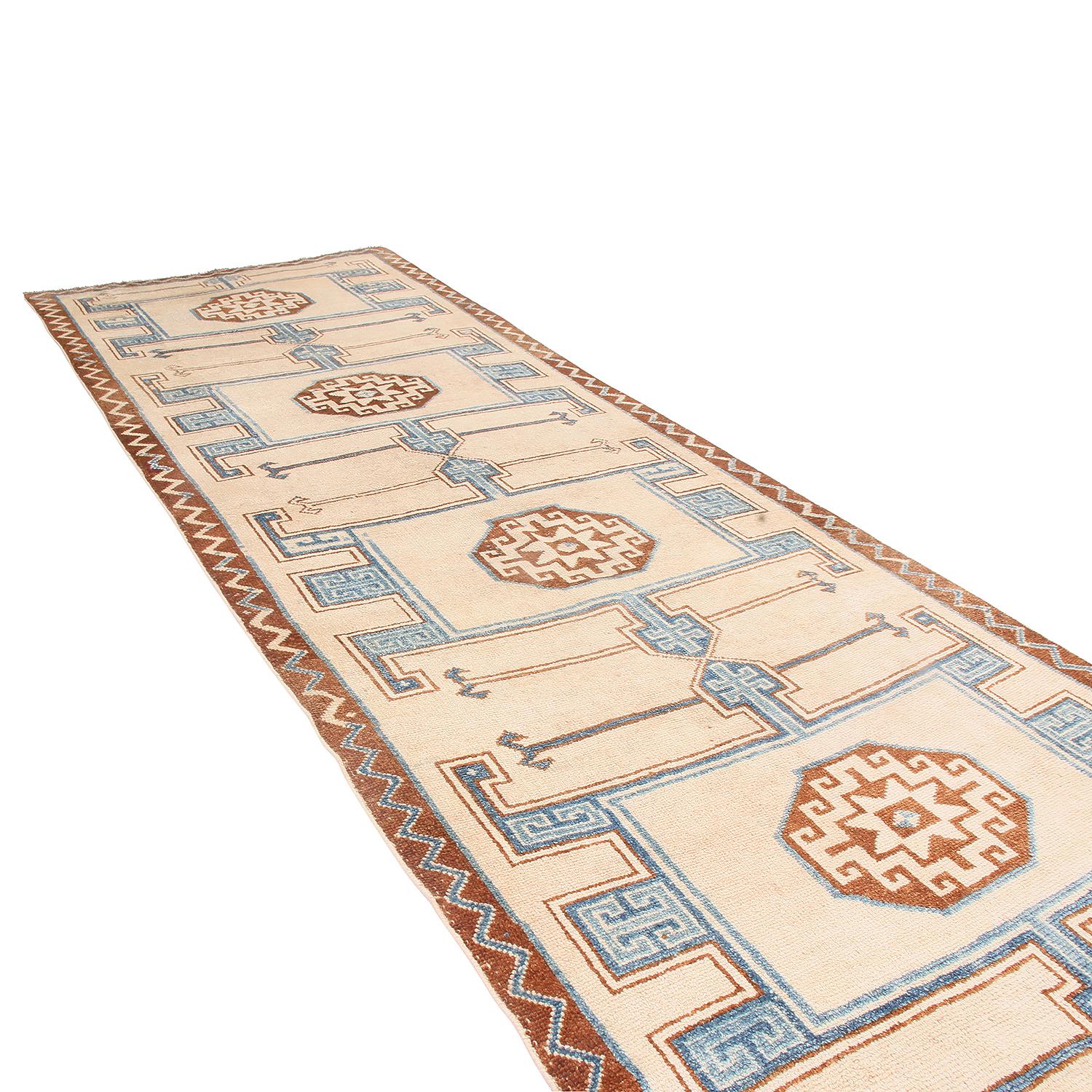 Hand knotted in wool originating from Turkey, this midcentury runner enjoys one of the most uncommon paginations of colorways in this design among its collection, an inviting marriage of artisan beige and cream background with frost blue and brown