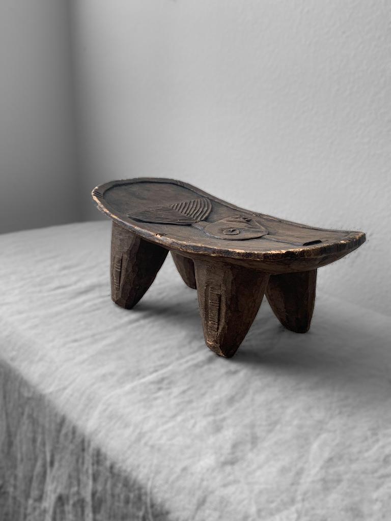 Einzigartiger kleiner afrikanischer Senofu-Hocker im Vintage-Stil, der durch einen in die Platte geschnitzten Stammeskrieger hervorgehoben wird. Es gibt einige Schrammen und Kratzer auf dem Hocker, die seinem Alter entsprechen und ihm eine sehr