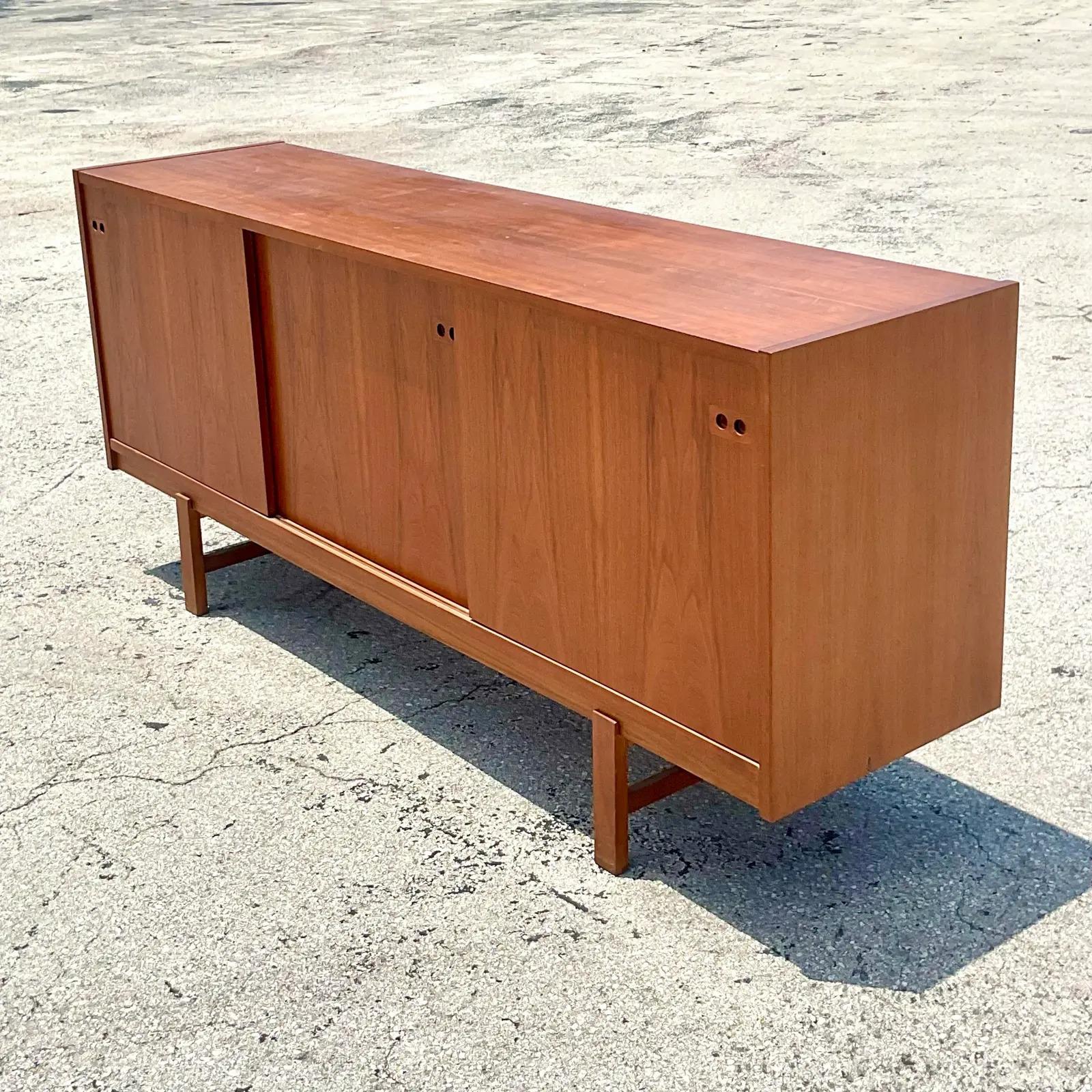 A vintage Midcentury Danish teak credenza. Made by the iconic Kofod Larsen. Beautiful wood grain detail with three sliding doors. Two sections with open shelving and a center section with sliding drawers. Unmarked. Acquired from a Palm Beach estate.