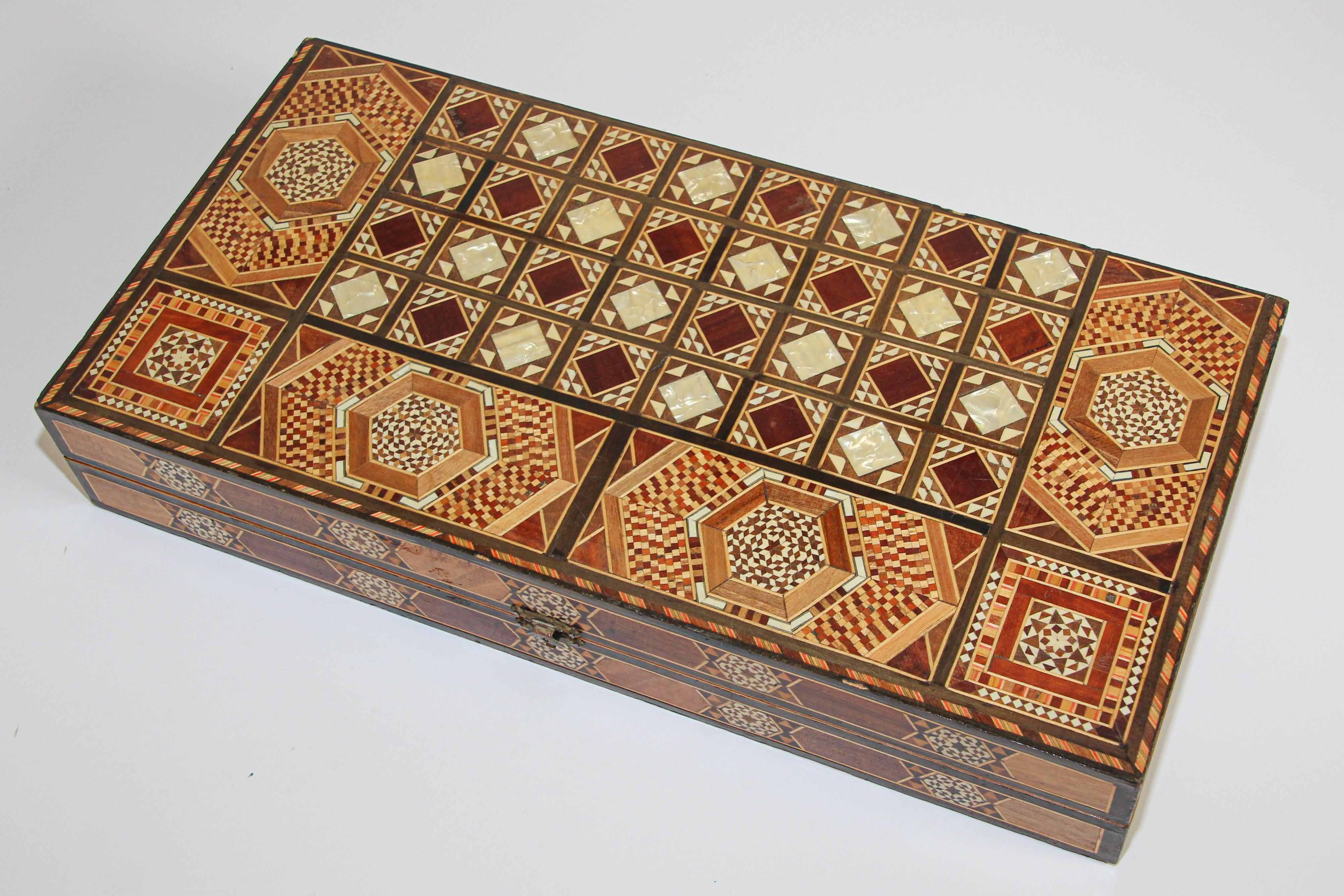 Large vintage midcentury Syrian inlaid with mother of pearl mosaic backgammon game.
Great inlaid micro mosaic hinged marquetry game box features a chess and checker board on the exterior and backgammon board on the interior with all the wooden dice