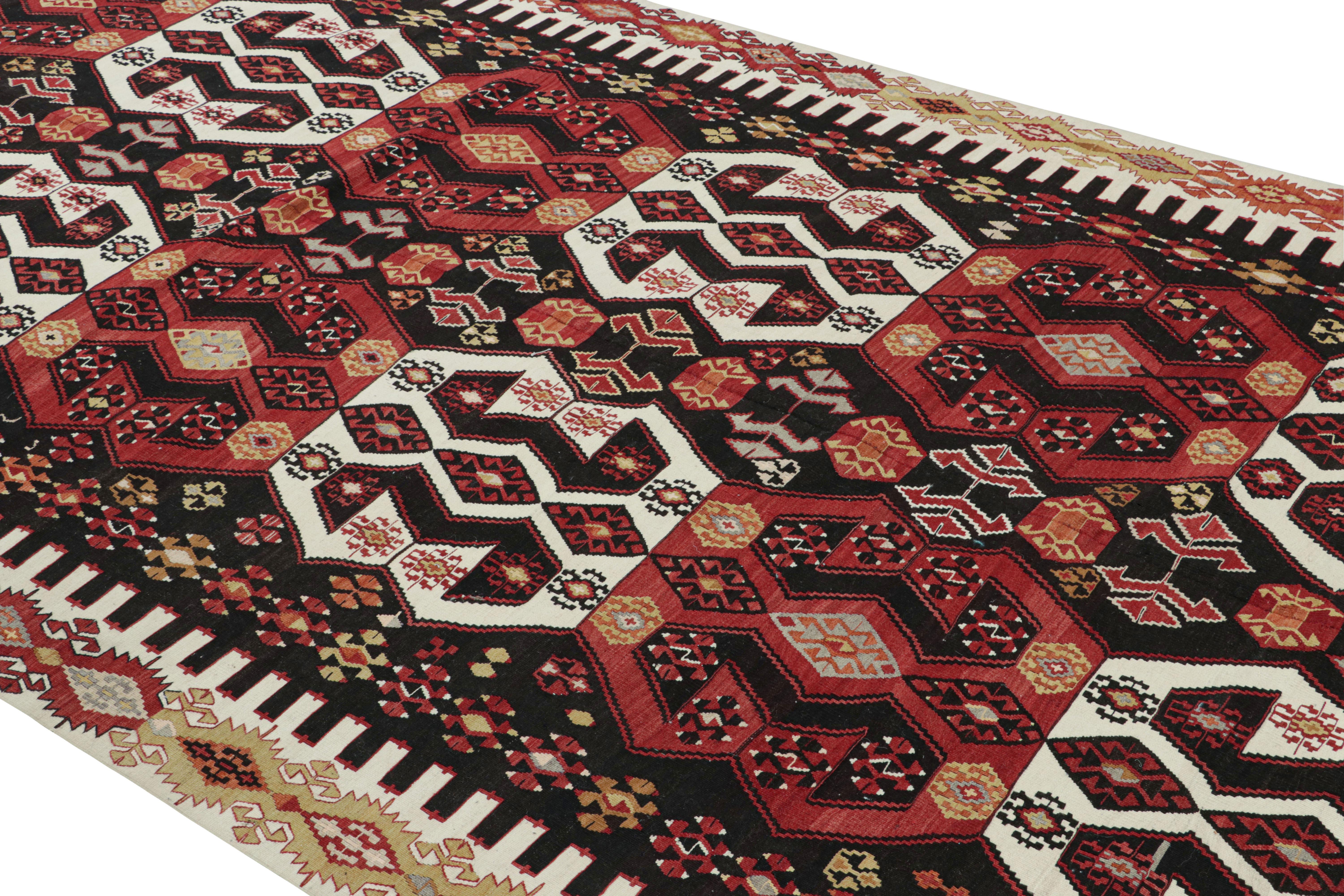 Flat-woven in Turkey originating between 1950-1960, this vintage midcentury geometric Kilim hails from the city of Malatya, enjoying a bold tribal contrast of its rich burgundy red and brown hues with the crisp off-white and soothing yellow tones