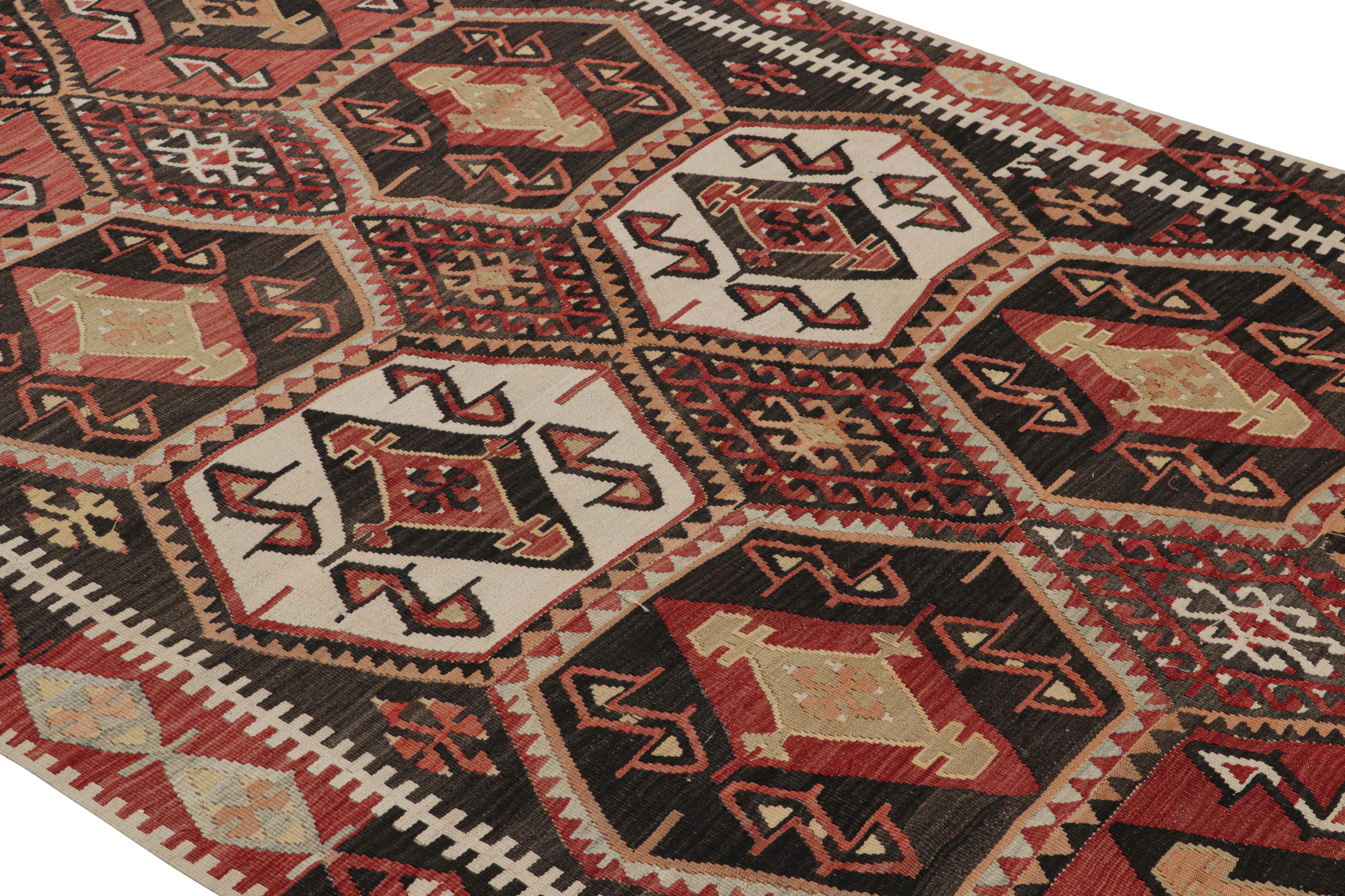 Flat-woven in Turkey originating between 1950-1960, this vintage midcentury geometric kilim hails from the city of Malatya, enjoying a bold tribal contrast of its rich burgundy red and brown hues with the crisp off-white and soothing yellow tones