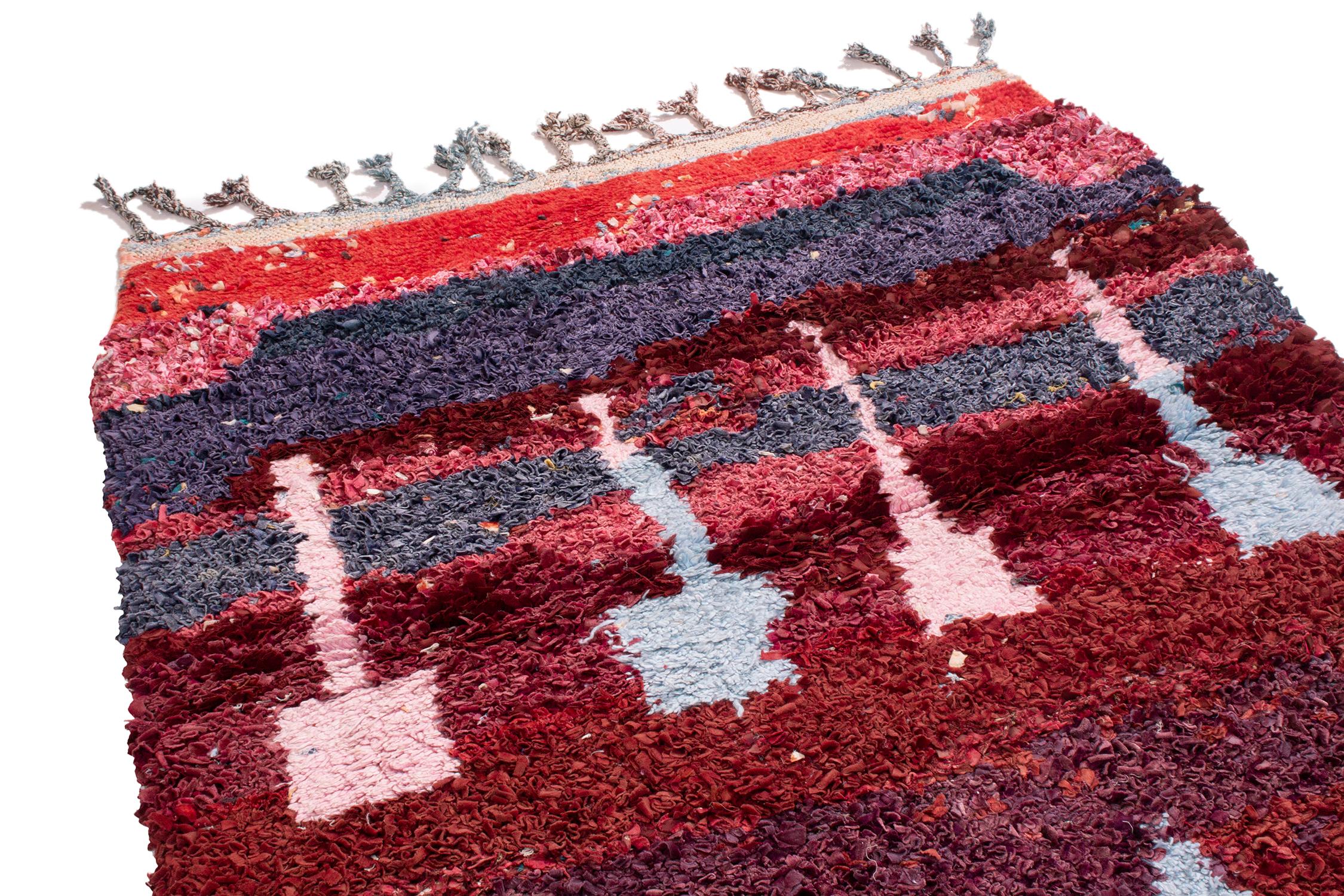 Originating from Morocco in the 1950s, this vintage midcentury Moroccan rug features lesser-known symbols of regional paternity in uniquely bright colorways. Crafted with a distinct background of burgundy red, midnight blue, Abrash pink, purple, and