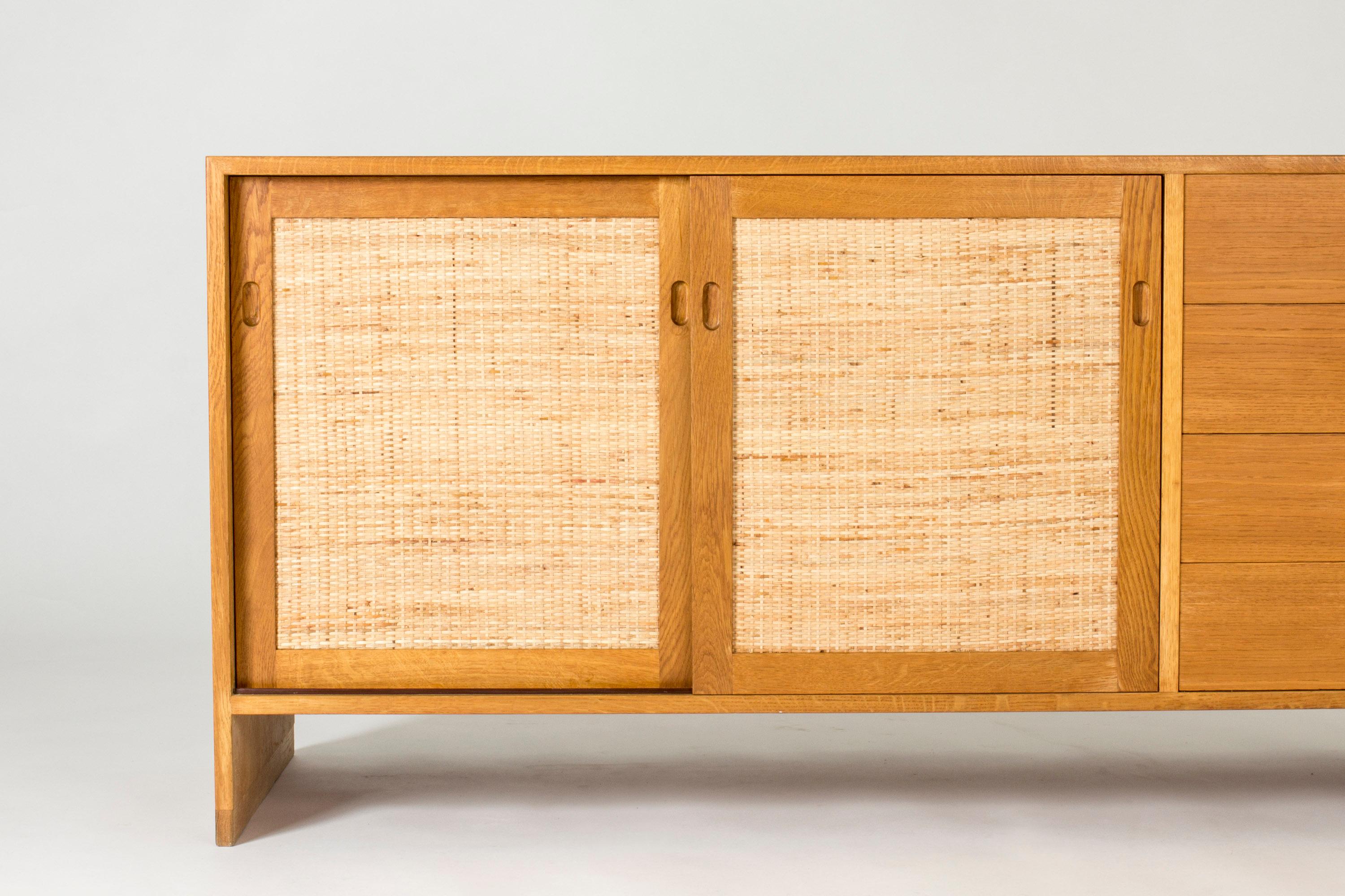 Oak sideboard by Hans J. Wegner, with rattan fronts and sculpted knobs on the drawers. The sides come down to form the legs, and give the sideboard a clean silhouette, contrasted by the round knobs and organic rattan.